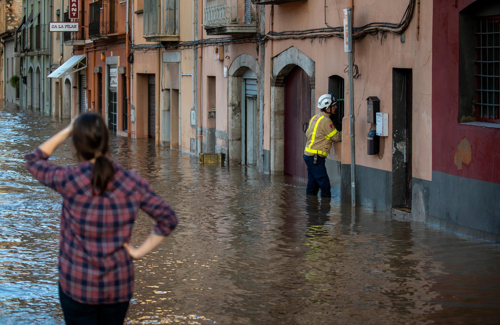 Räddningspersonal talar med en person i ett översvämmat hus.