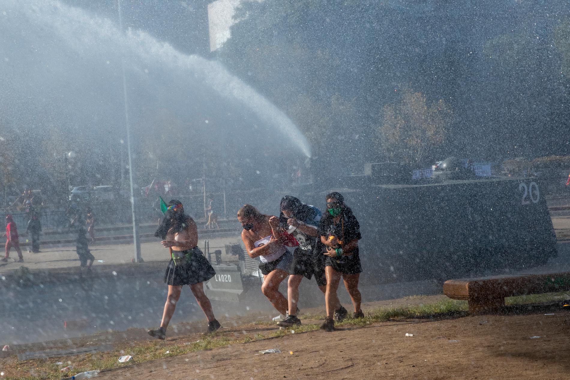 Demonstranter springer från polisens vattenkanon i Chiles huvudstad Santiago på den internationella kvinnodagen den 8 mars.