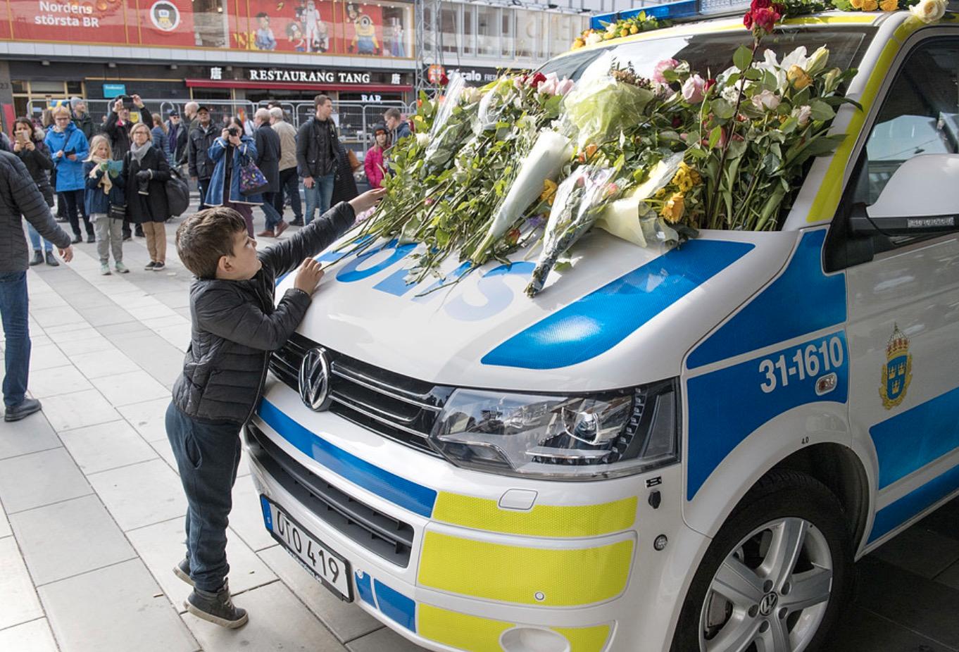 En liten pojke placerar blommor på en polisbil vid Sergels torg i Stockholm.
