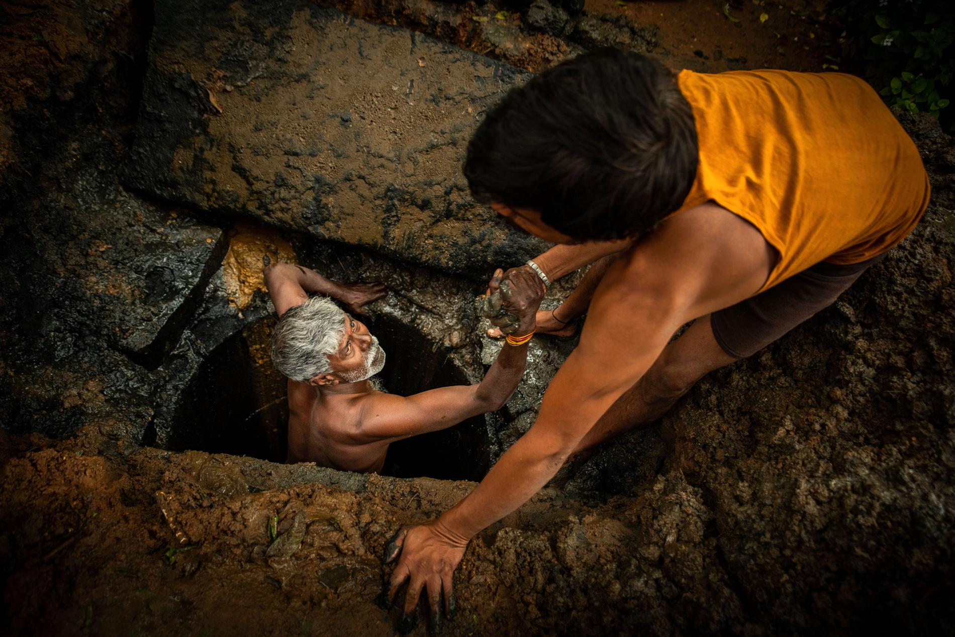 54-årige Kaverappa från Bangalore, Indien, hjälps upp ur latrinhålet han håller på att tömma av en kollega. Kaverappa har arbetat som latrintömmare i 35 år.