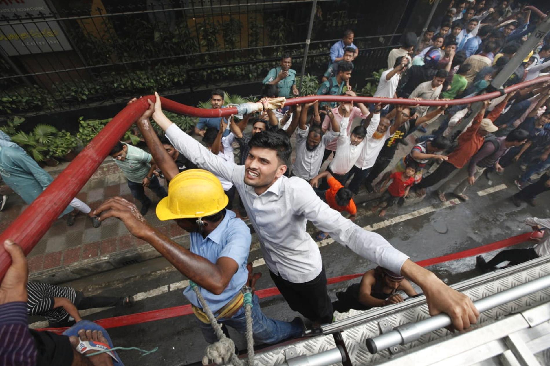 Lokalbefolkning hjälper brandkåren att bekämpa den jättebrand som härjar ett kontorshus i Dhaka i Bangladesh.