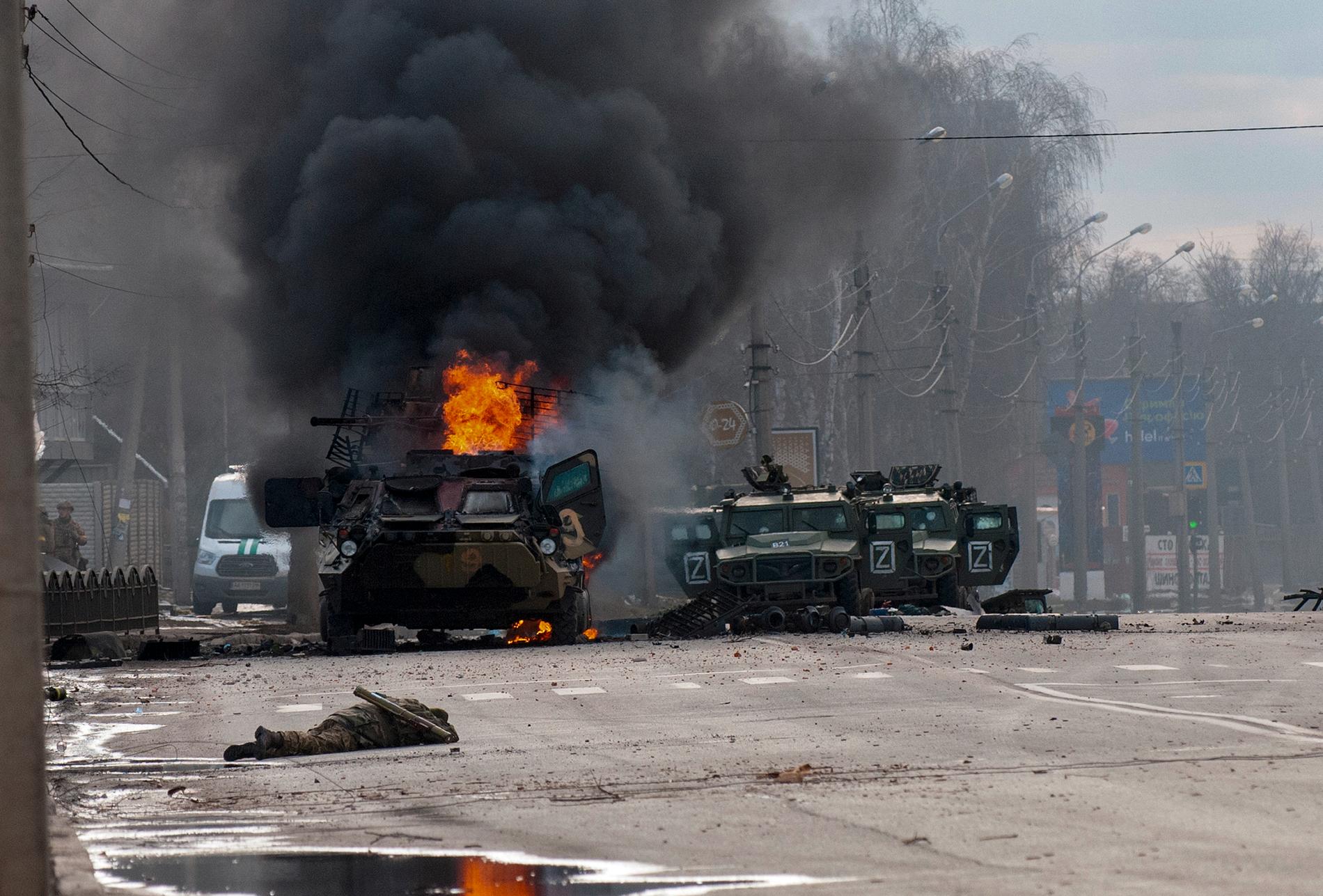 En rysk soldat ligger död på gatan i Charkiv. Bakom en brinnande stridvagn.