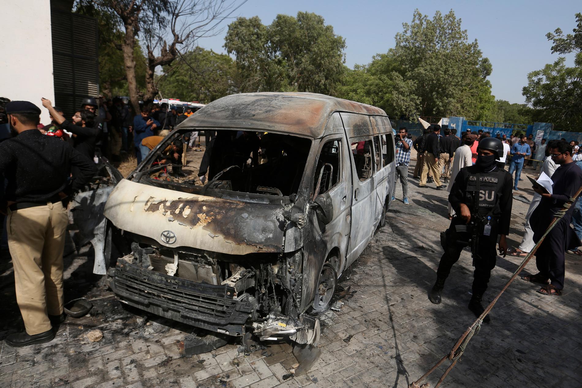 Pakistansk polis undersöker den utbrända minibussen efter självmordsattentatet.