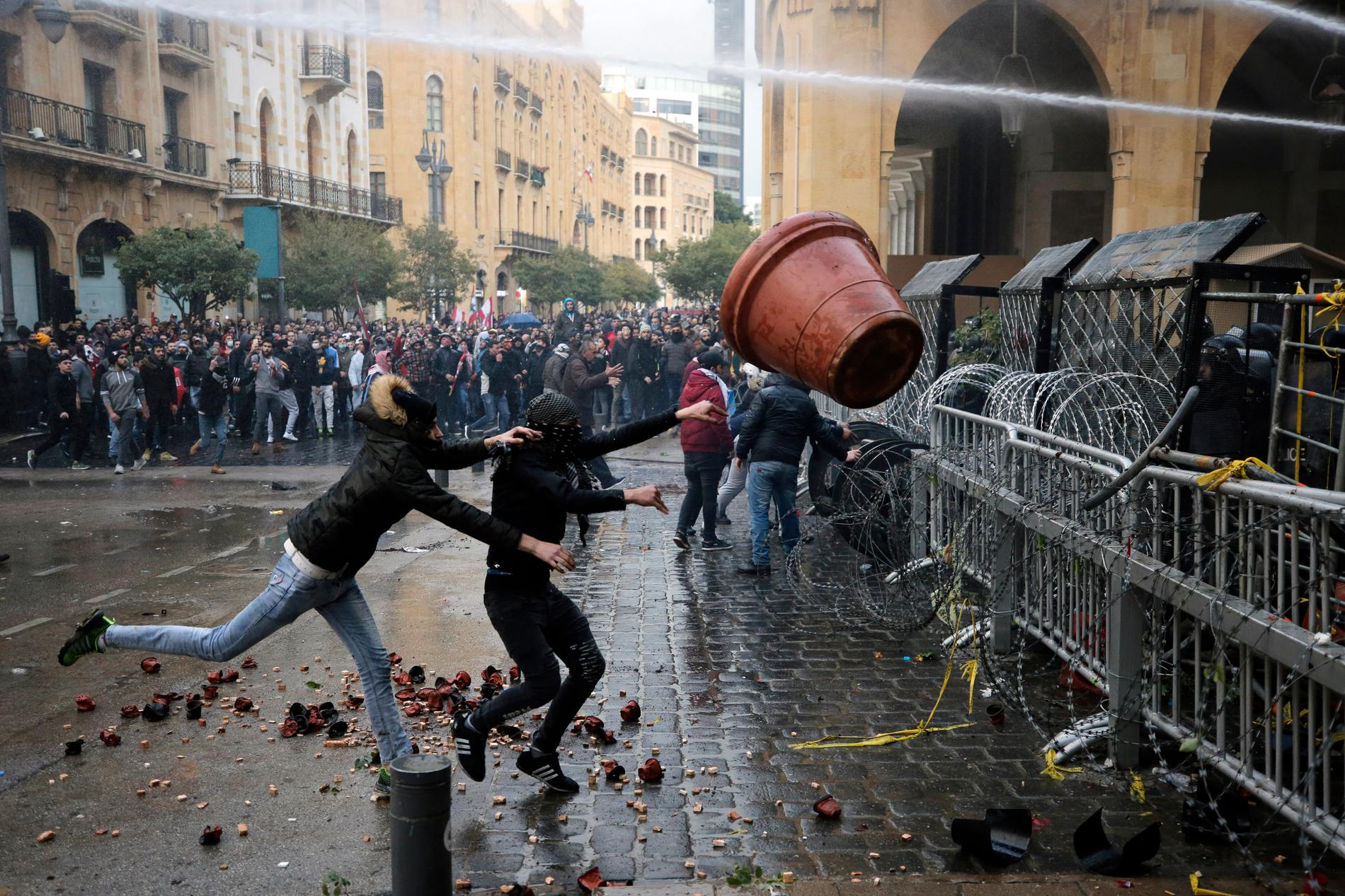 Demonstranter hivar en stor blomkruka mot poliser bakom en avspärrning vid parlamentet.
