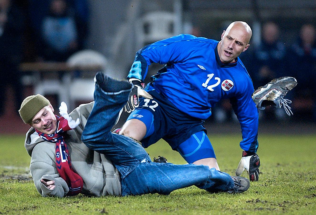 Norska supportern Henrik Hægeland tacklas omkull av landslagsmålvakten Frode Olsen.