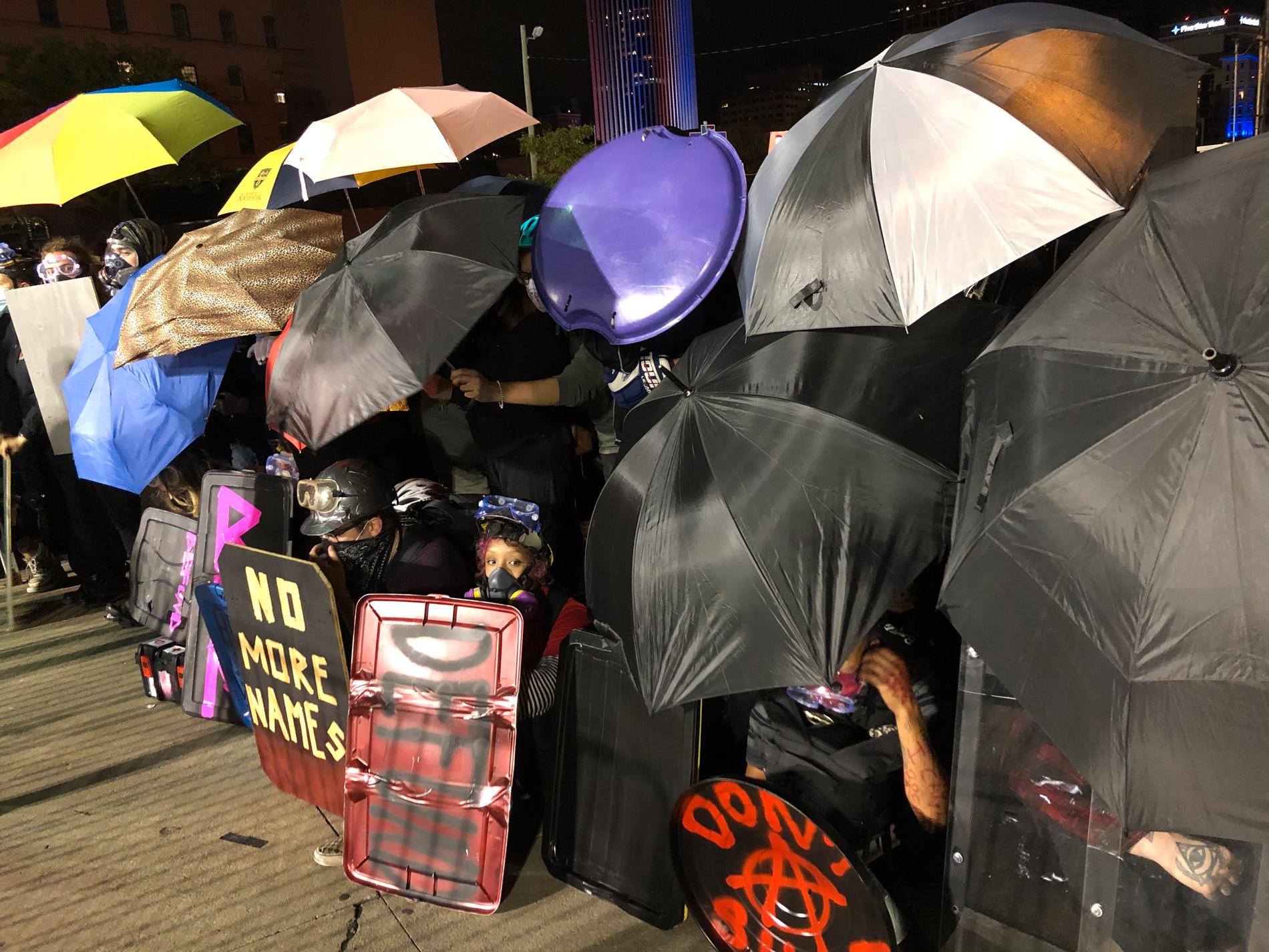 Demonstranter bildar en mur av paraplyer, plywood och pulkor.
