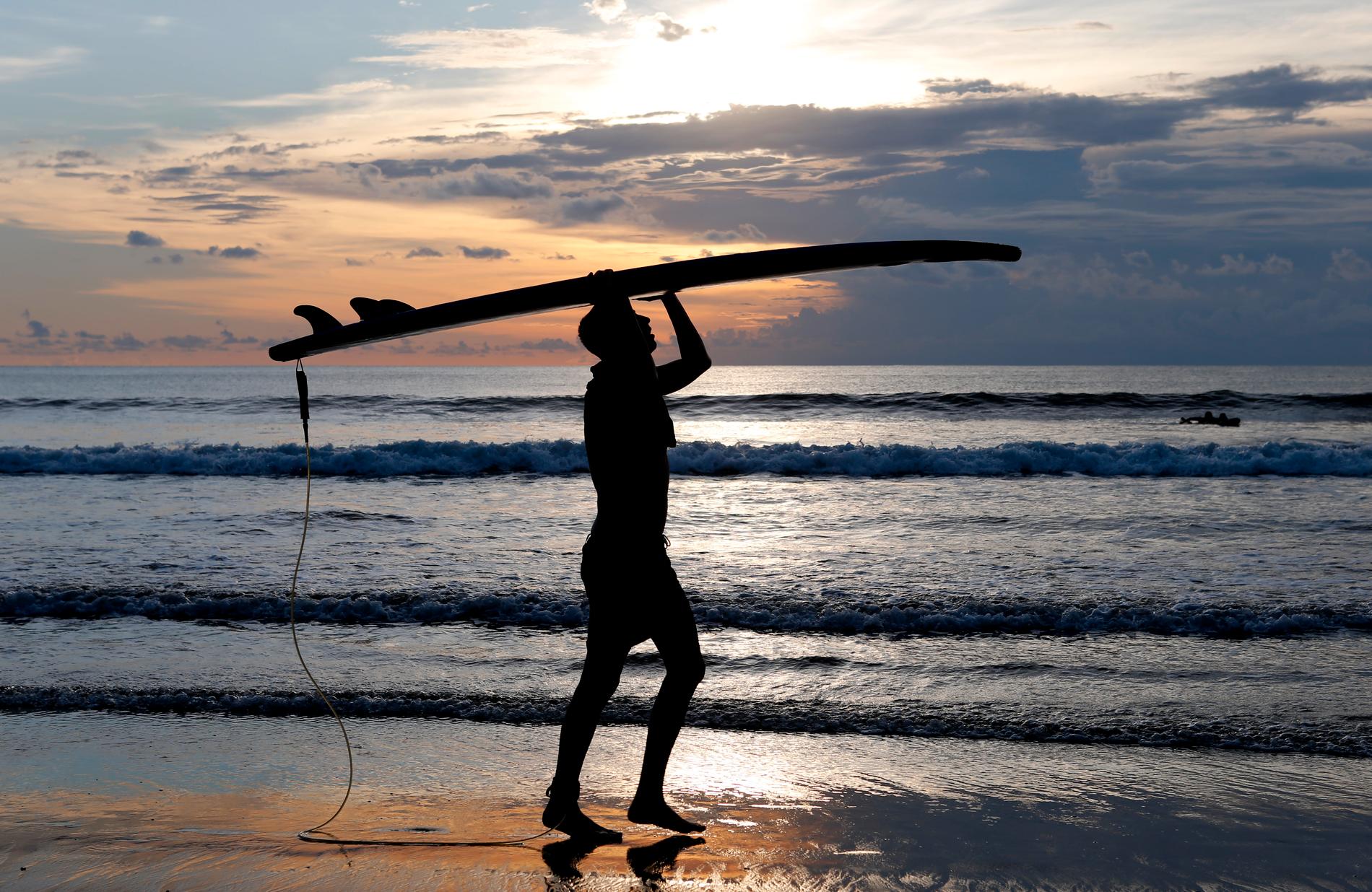 En surfare bär sin bräda på en strand på Bali i mars. Arkivbild.