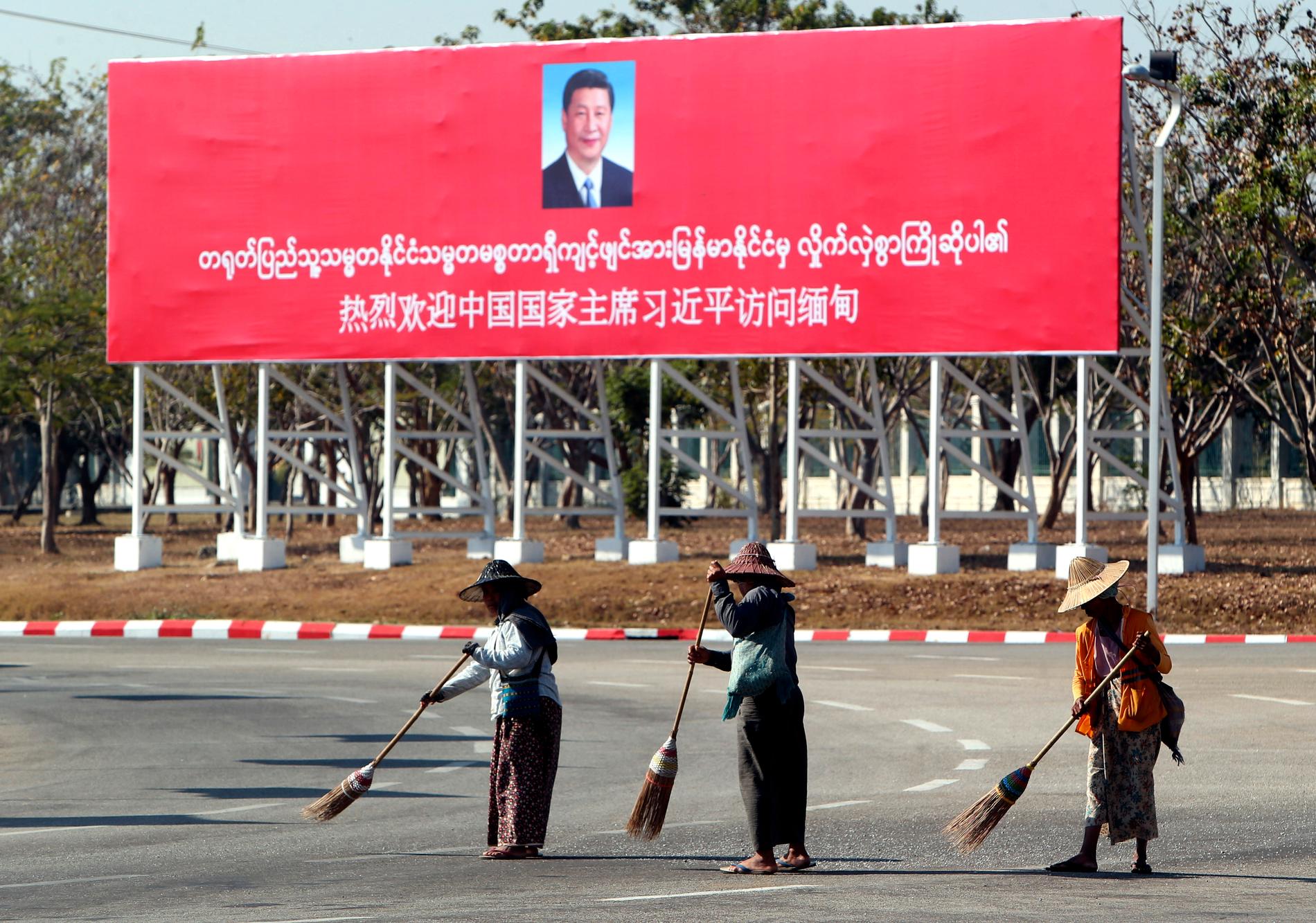 Gatan sopas framför en stor banderoll som välkomnar Xi Jinping till Myanmar.