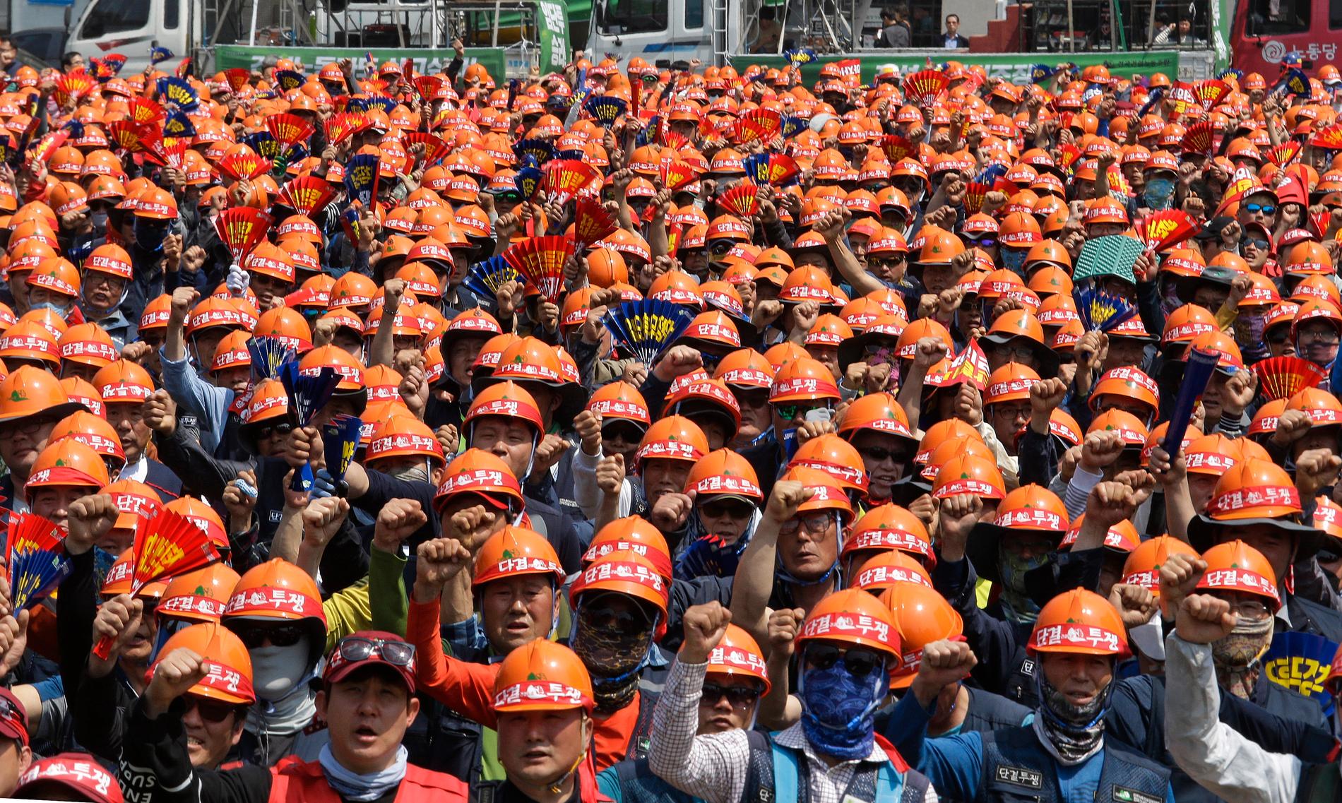 Ett hav av arbetare samlas i Sydkoreas huvudstad Seoul. På hjälmarna står "förenas, och kämpa".