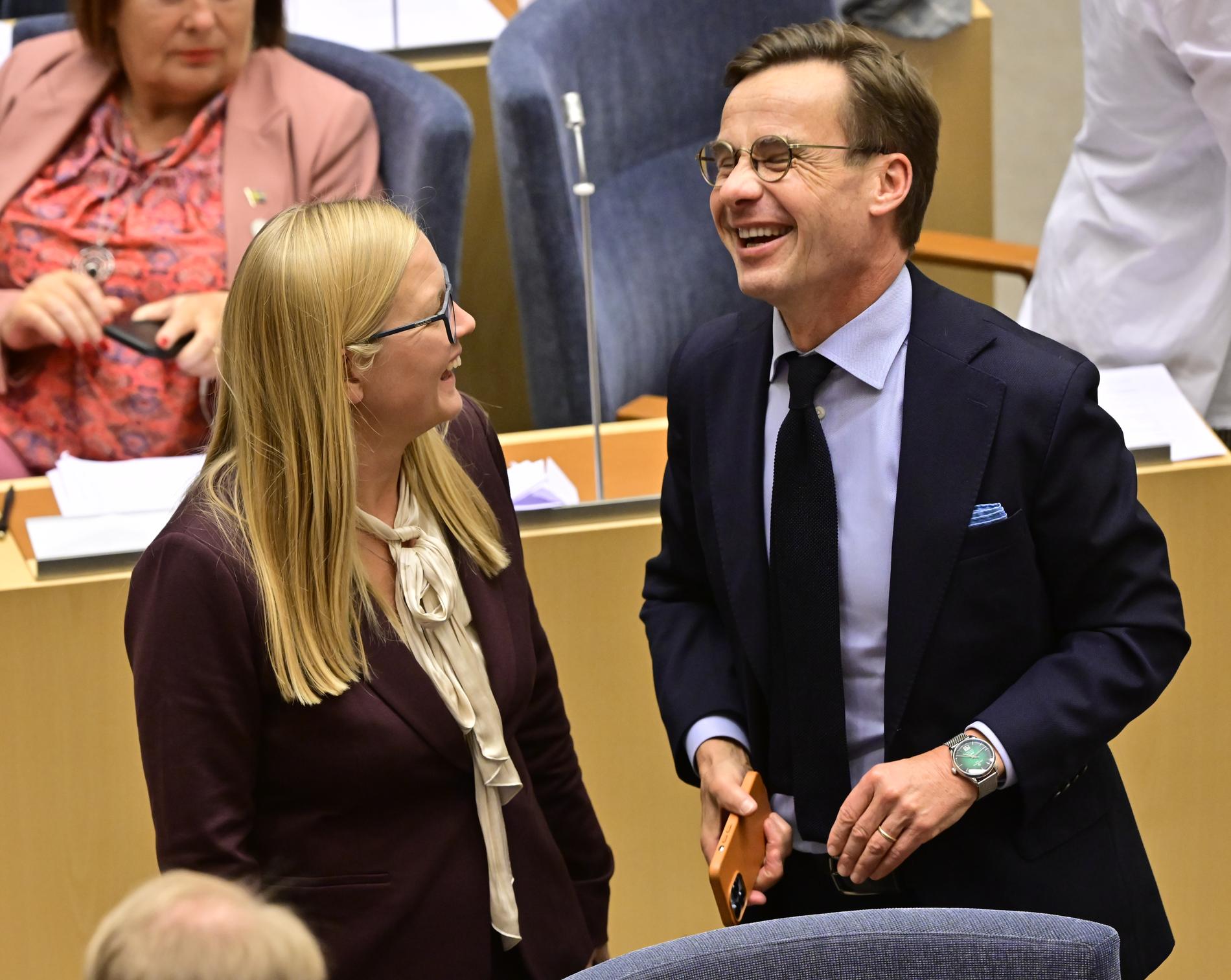 Nyvalda andra vice talman Julia Kronlid (SD) skrattar ihop med Moderanternas partiledare Ulf Kristersson i riksdagens kammare.