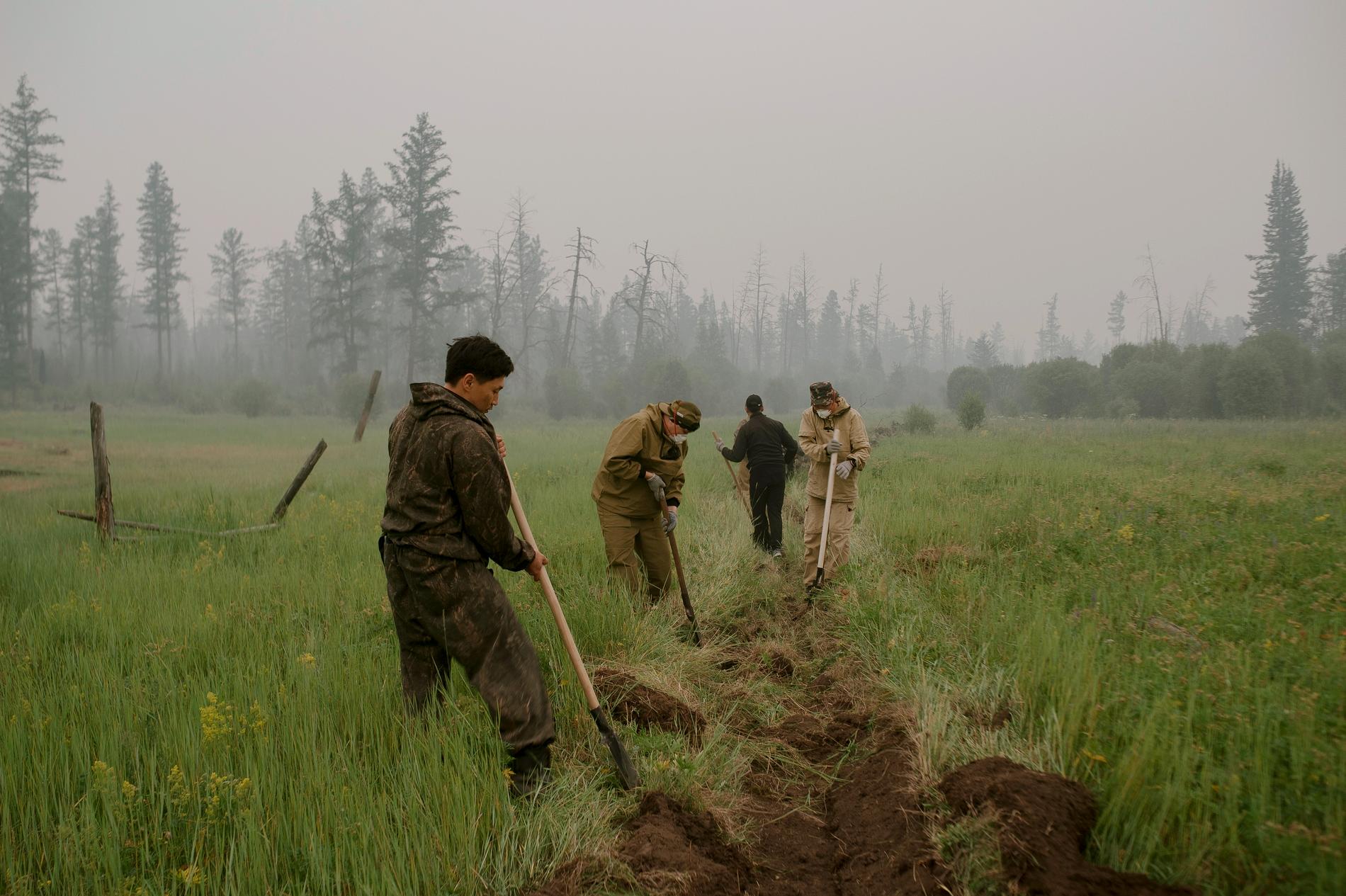 Frivilliga hjälper till med att gräva brandgator och kväva eldrester i den pyrande marken den 20 juli.