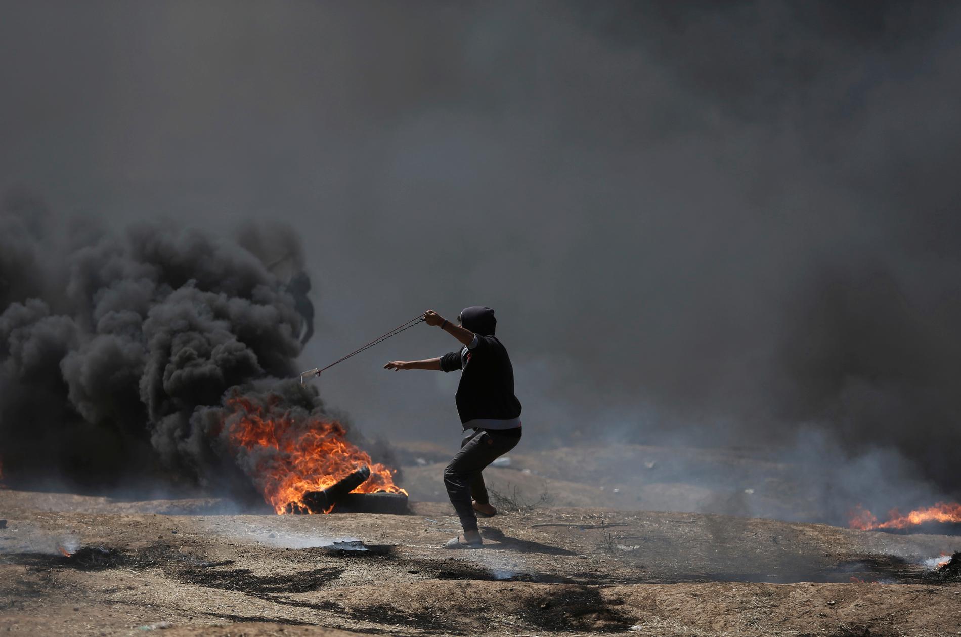 En palestinier slungar stenar mot israeliska styrkor på andra sidan gränsen, vid protesterna på Gazaremsan inför invigningen av USA:s ambassad i Jerusalem.