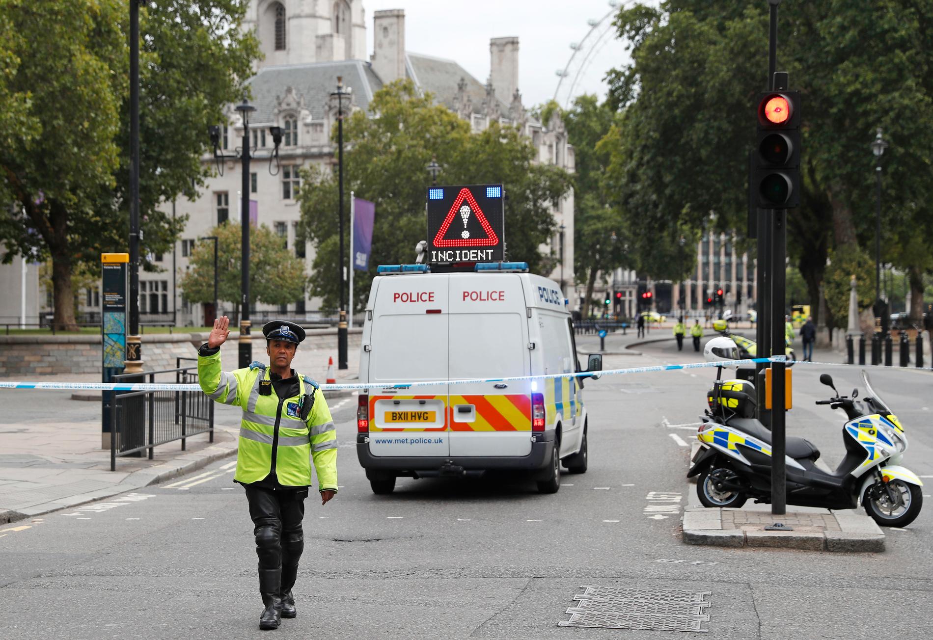 En polis gestikulerar utanför avspärrningarna vid en gata i centrala London, efter det att en bil kraschat in i en säkerhetsbarriär utanför det brittiska parlamentet.
