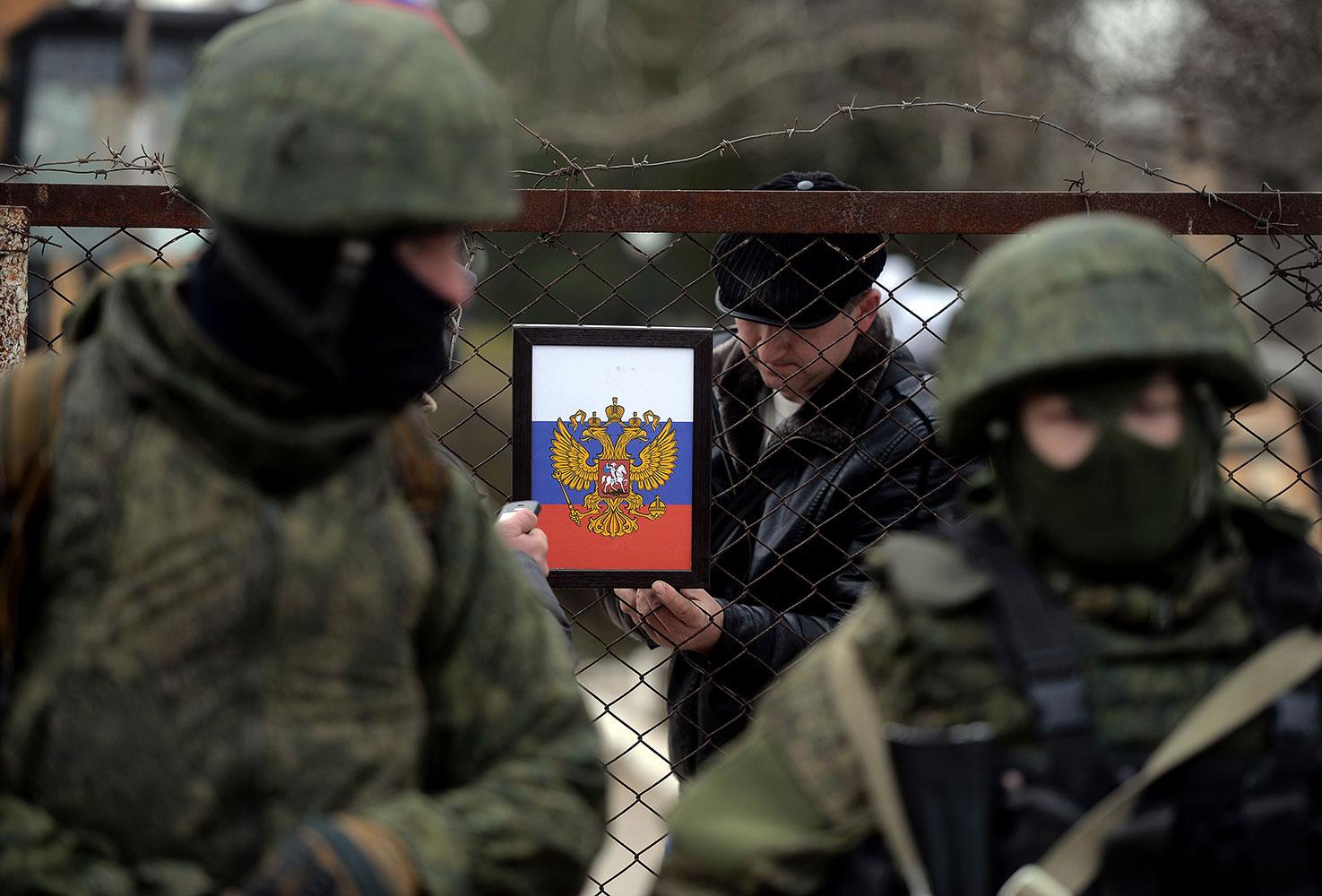 En man sätter upp den ryska örnen vid en checkpoint på Krim. I förgrunden ryska soldater.