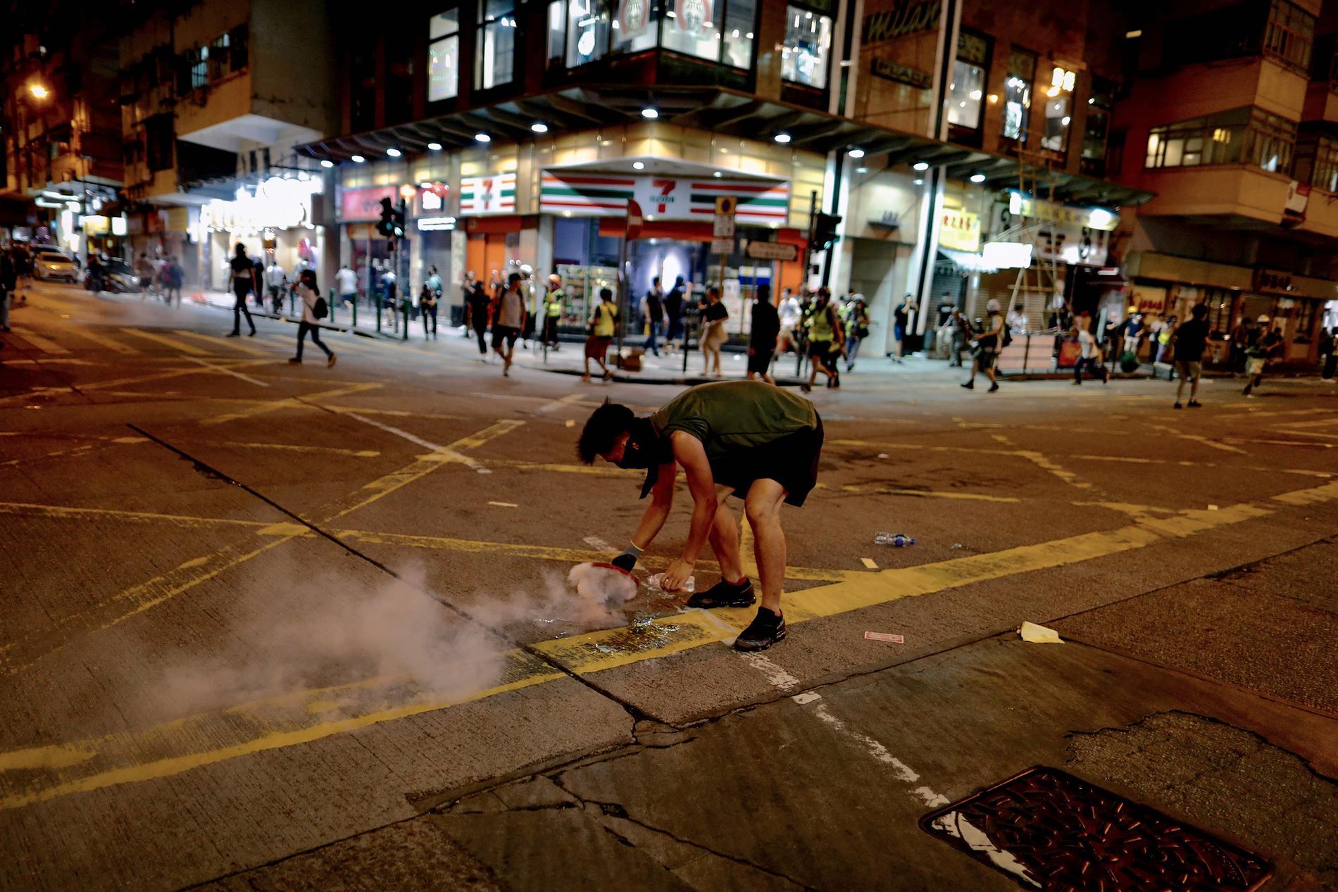 En demonstrant försöker täcka över en tårgasgranat under gatuprotesterna mot hårt kinesiskt styre i Hongkong..