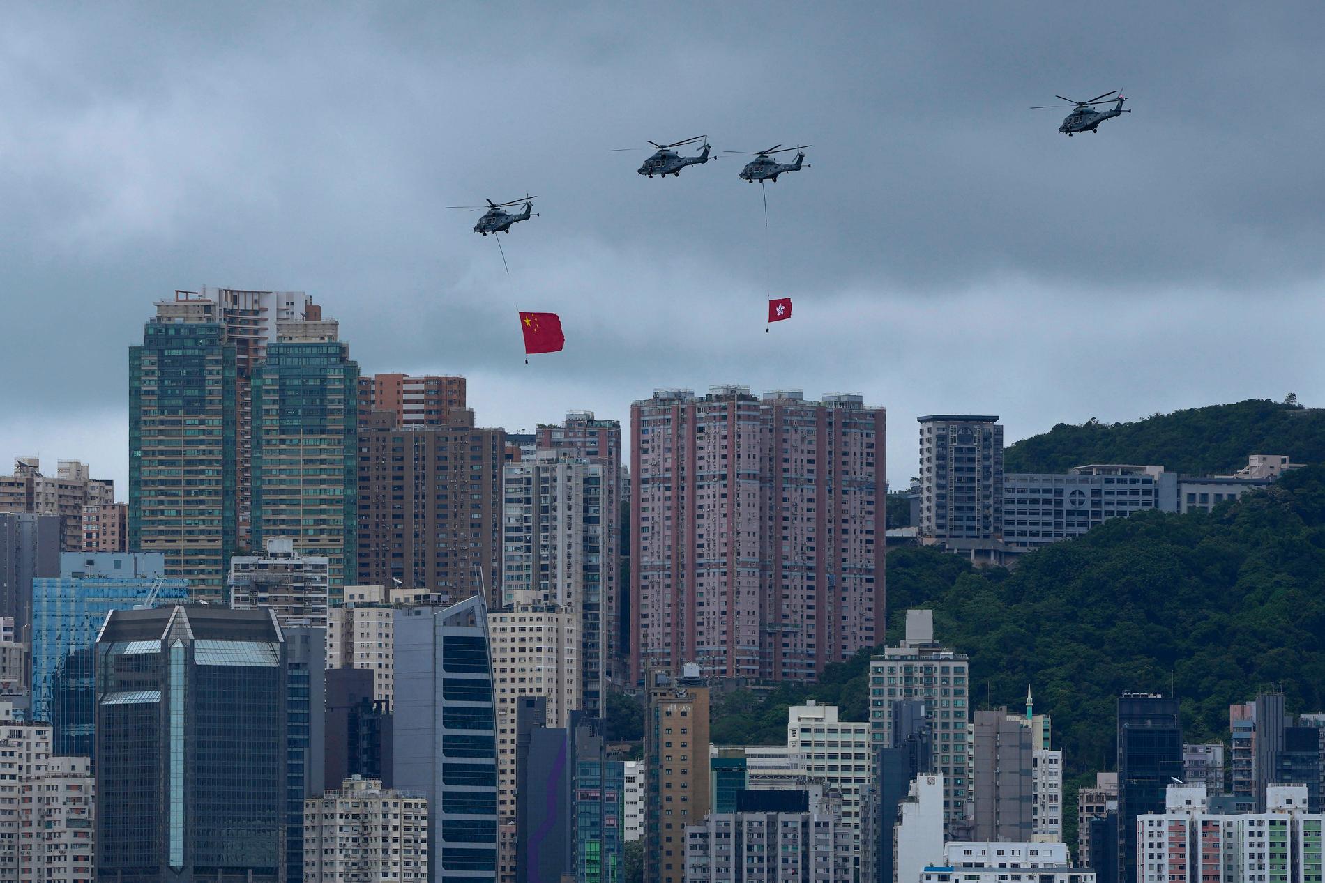 Helikoptrar flyger fram över Hongkong med två flaggor: en stor kinesisk och en mindre Hongkong-flagga.