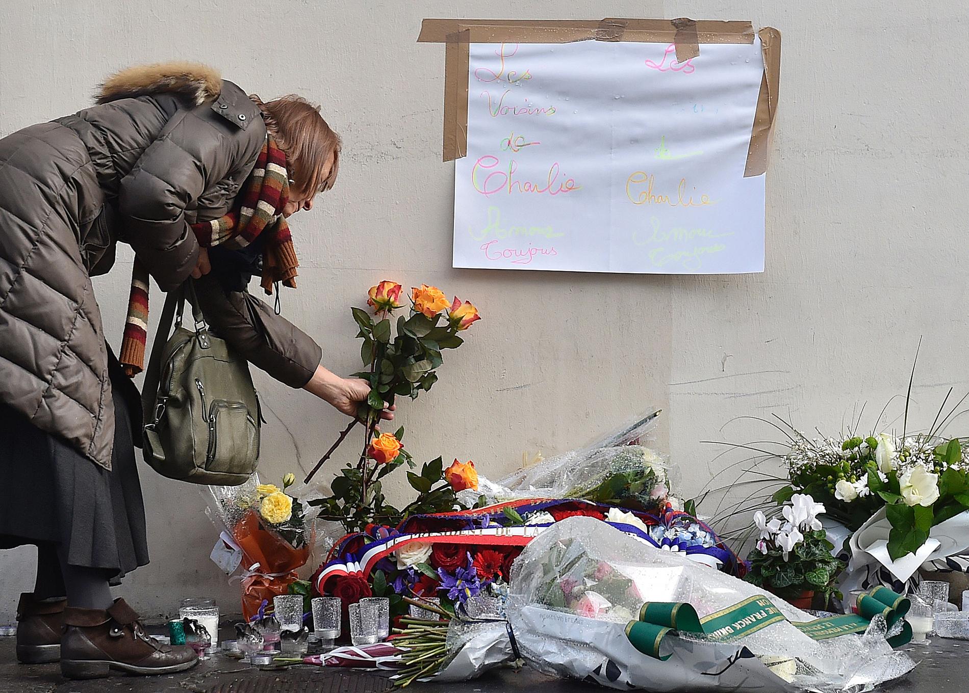 En kvinna lägger blommor framför satirtidningen Charlie Hebdos redaktion i Paris på årsdagen av attacken.