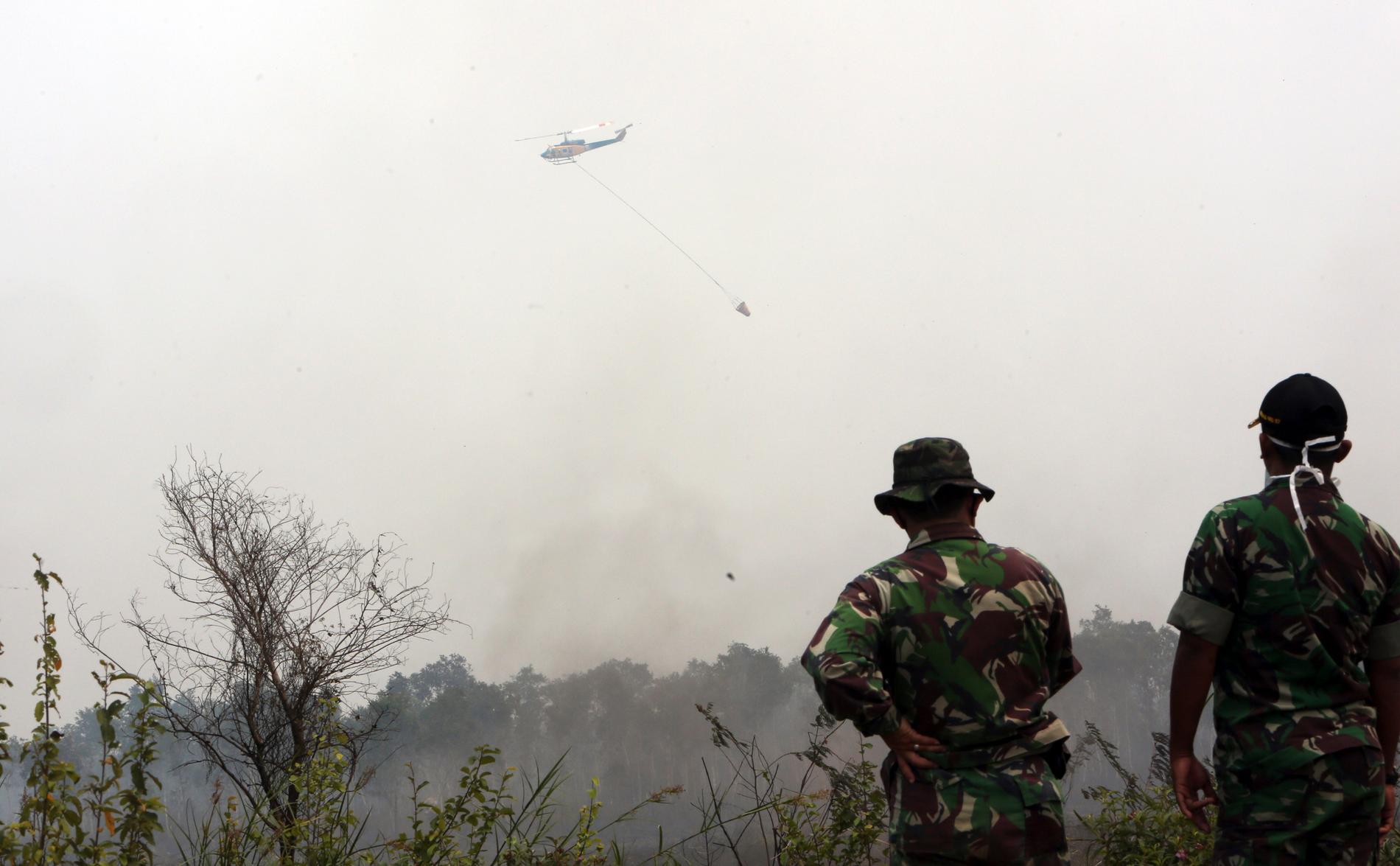 Två militärer ser på när en helikopter vattenbombar en skogsbrand på södra Sumatra 2015. Arkivbild.