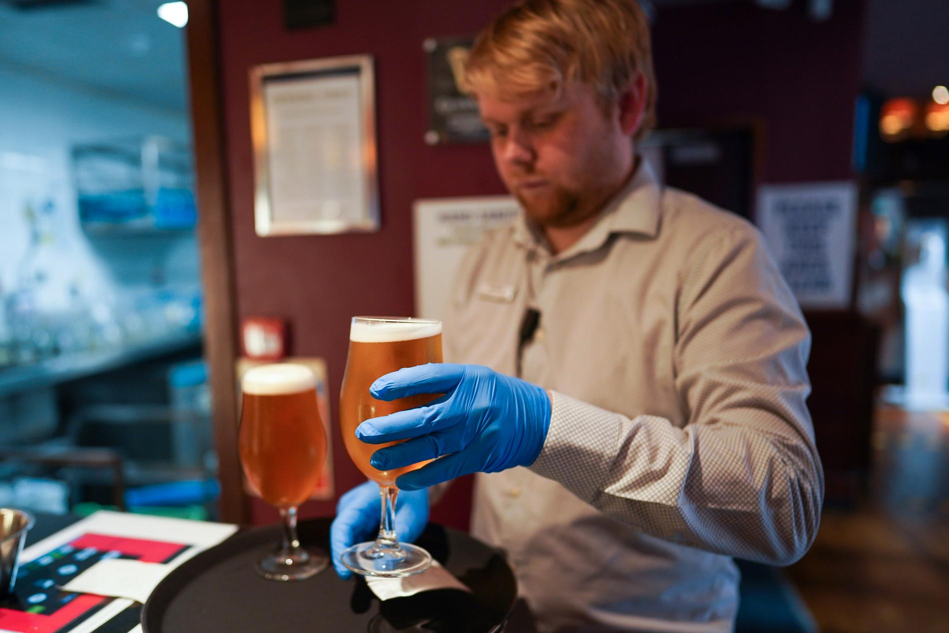 Bartendern på Job Bulman pub i Newcastle använder plasthandskar när han fyller ölglasen, England