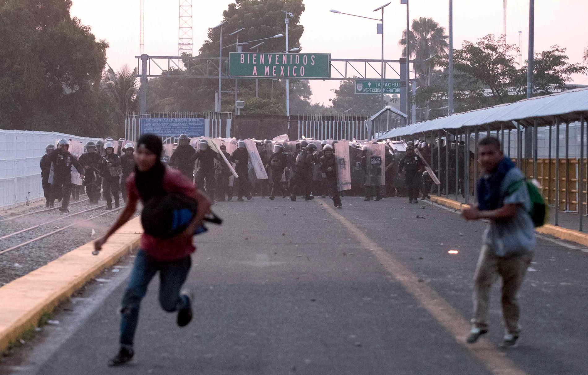 Migranter flyr från mexikanska poliser vid en sammandrabbning på en bro som binder samman Mexiko och Guatemala.