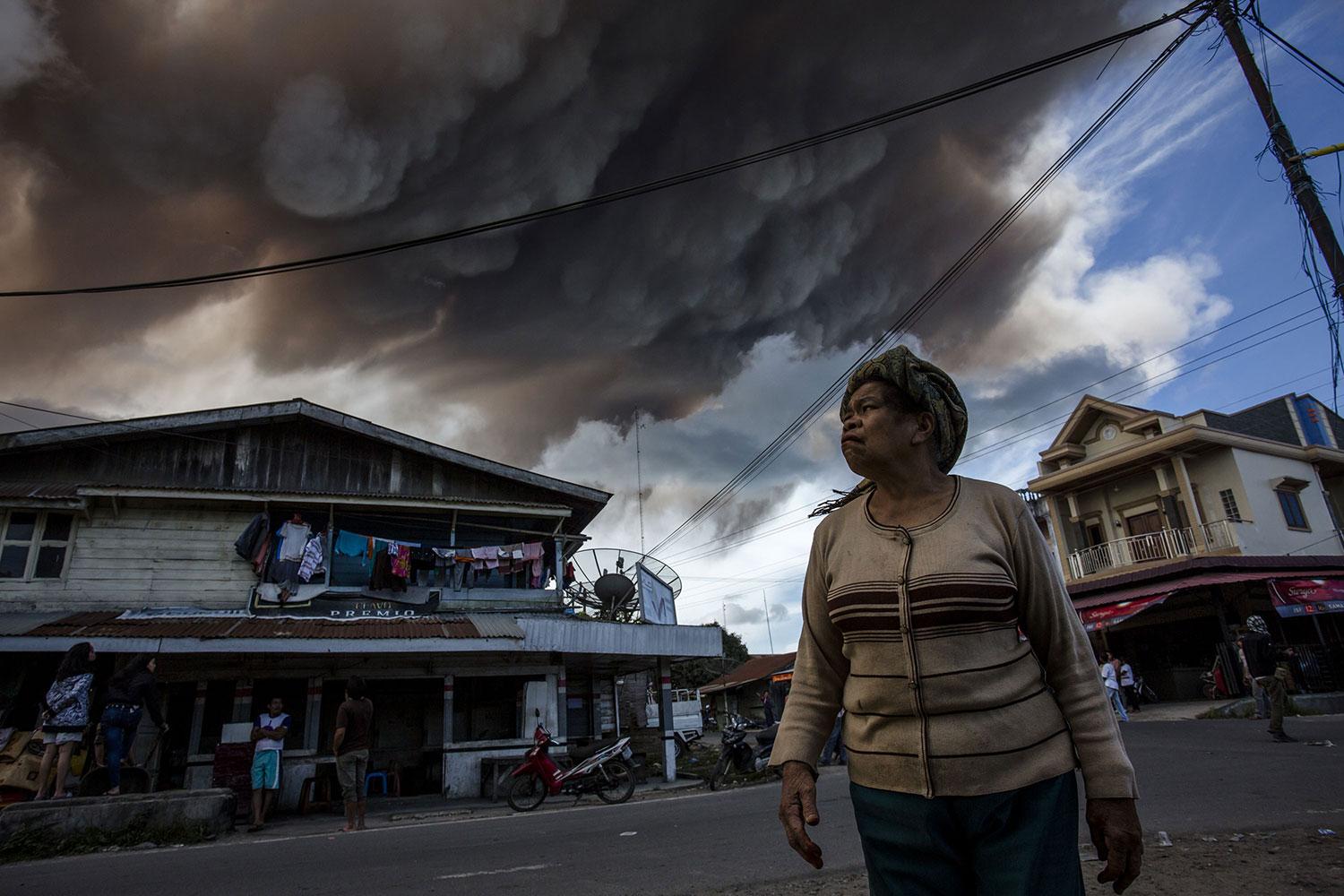 En kvinna tittar på ett stort rökmoln från vulkanen i byn Simpang Empat.