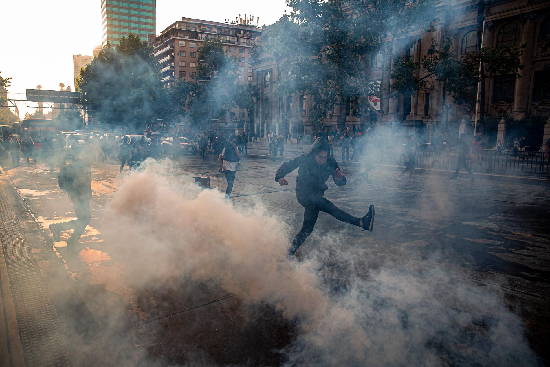 En demonstrant sparkar på en tårgasgranat under fredagens protester i Santiago.