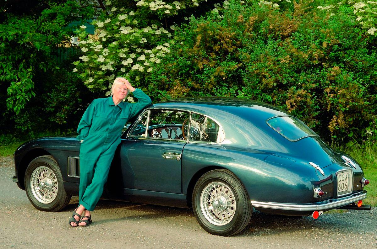Birgitta Stenberg framför en Aston Martin, iklädd overall och sandaler, precis som när hon mekade med sin egen Aston som ung. Just denna bil har faktiskt samma motor som satt i Birgittas. – Kamkedjan började skramla. Och eftersom gamla sportbilar var billiga, men reservdelarna dyra, så plockade jag i en Jaguarmotor i stället. Originalmotorn blev stående i ett garage hos en bekant, som många år senare sålde den vidare till en behövande. I Birgittas böcker ”De frånvända”, ”Chans”, ”Spanska trappan” och ”Skurkar” finns många fina bilupplevelser. De är samtidigt berättelser om denna nyfikna, sportbils-mekande, bisexuella, blondins brokiga liv i 1950- och 60-talets Europa.