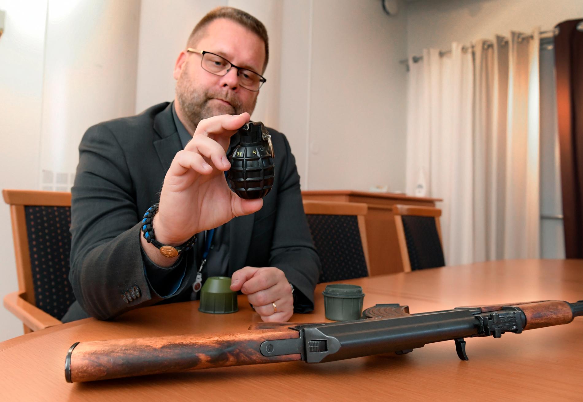 Polisens utredare Lars Bröms med en handgranat av den typ som dödade 63-åringen i Vårby gård i februari. Bredvid honom ligger en kalasjnikov – ett vapen som är vanligt förekommande i skjutningar.