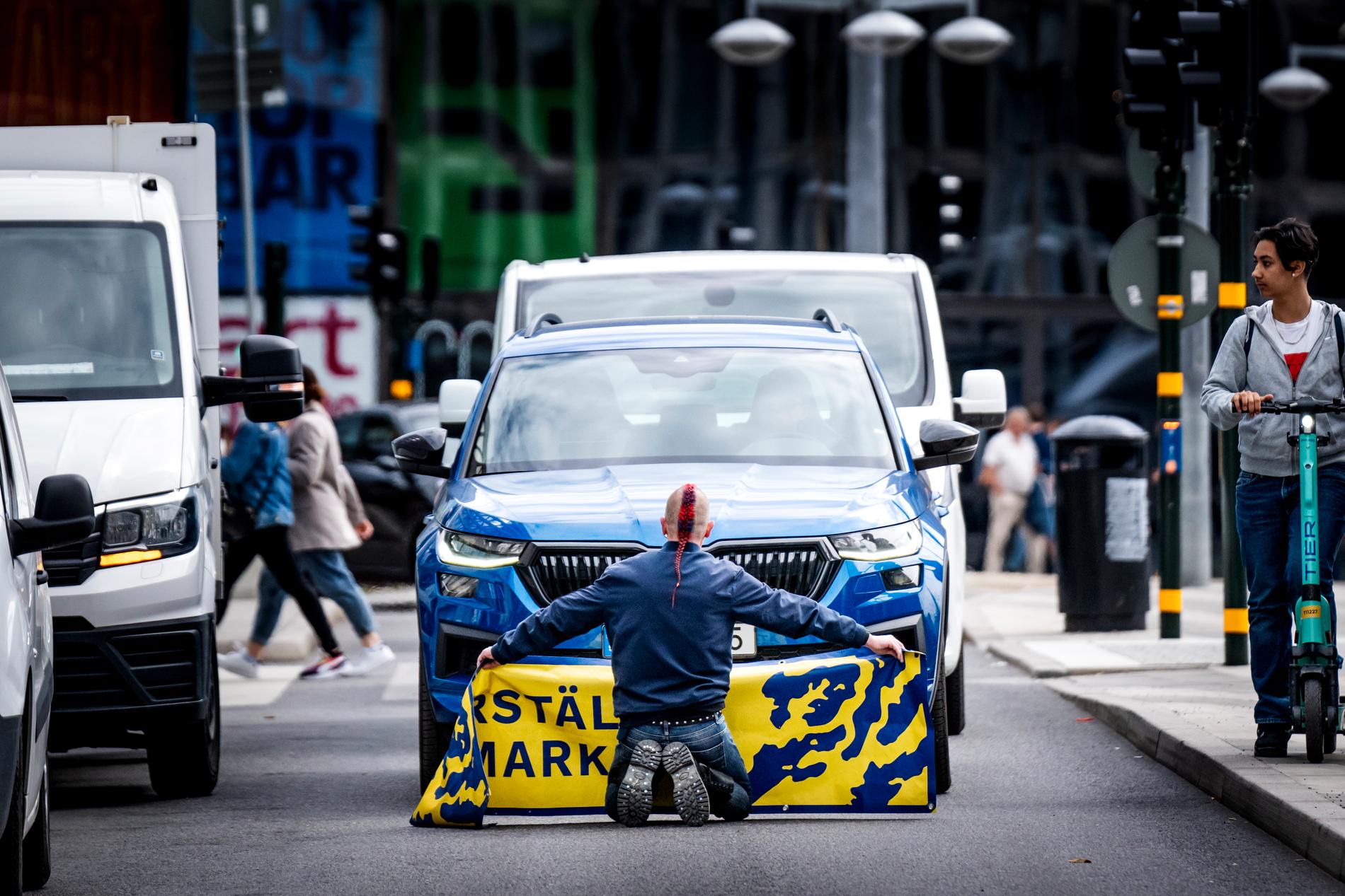 En klimataktivist med banderollen ”Återställ våtmarker” blockerar biltrafiken på Sveavägen vid Sergels torg i Stockholm den 7 juni 2022.