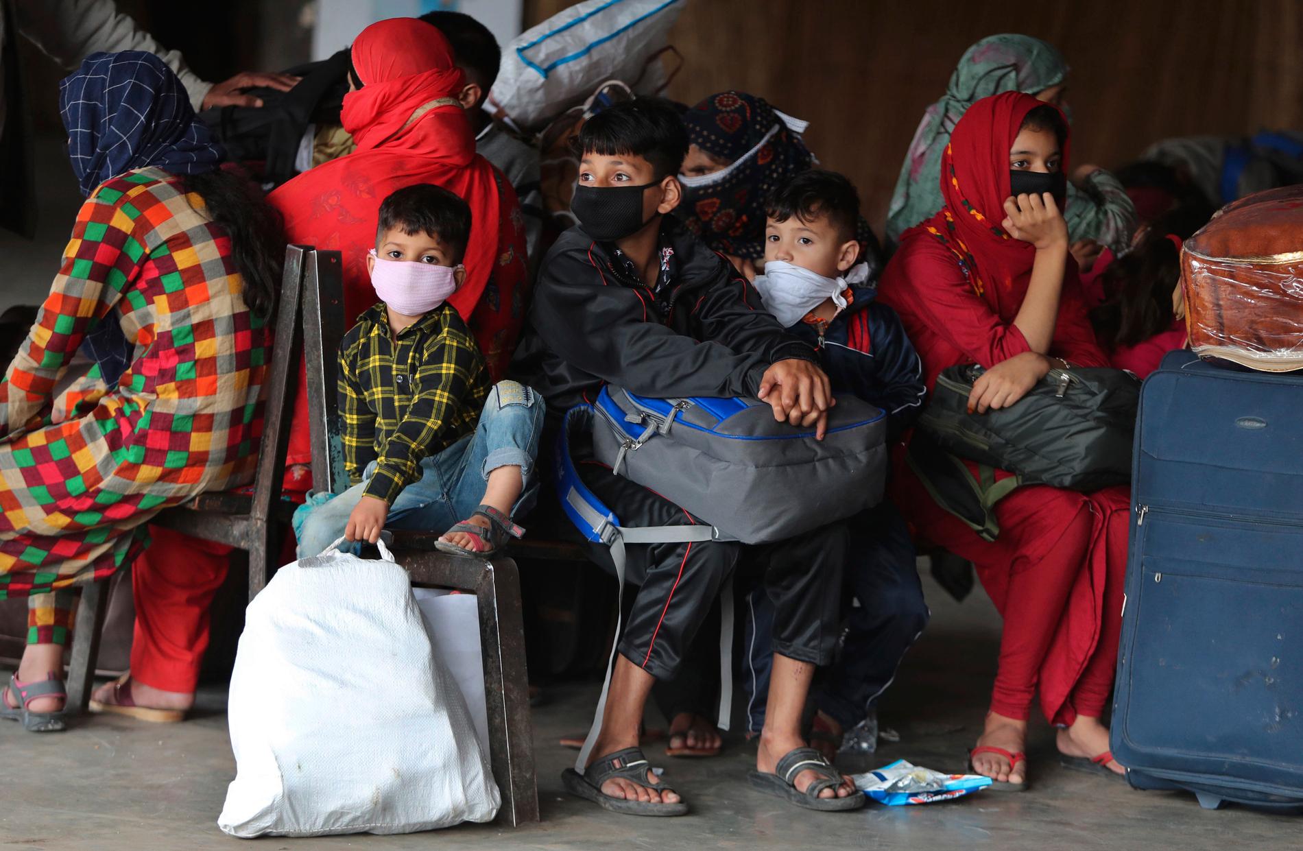 JAMMU, INDIEN Barn med munskydd väntar tillsammans med vuxna vid busstation i Jammu.