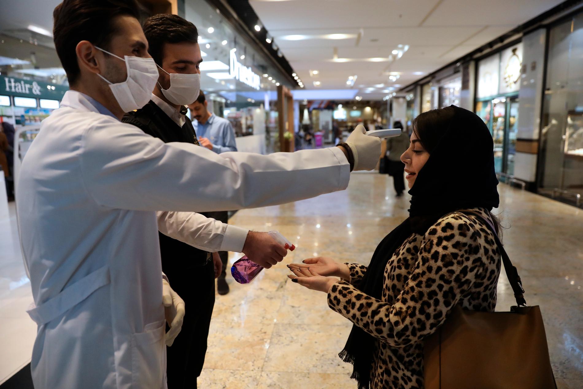 En kvinna får temperaturen mätt i ett köpcentrum i Teheran. Över 54 000 fångar släpps för att minska risken för smittspridning i landets fängelser.