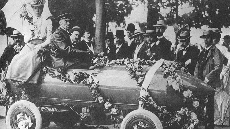 1899 passerade belgaren Camille Jenatzy hundrakilometersvallen för bilar. Bilen drevs av el och hette Aldrig Nöjd. Jenatzy kallades Den Röde Djävulen för sitt röda skägg.