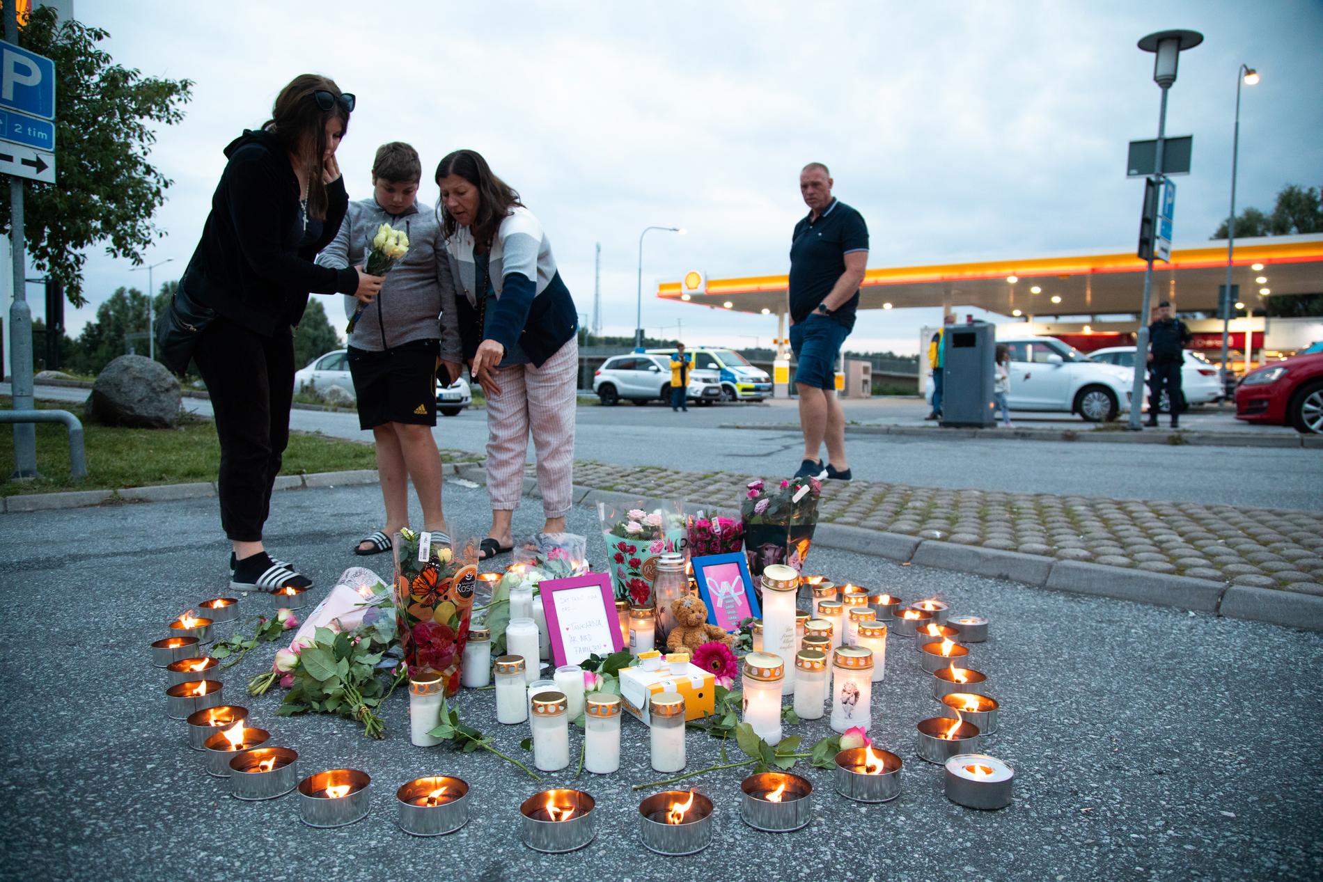 Människor tänder ljus och lägger blommor på platsen där en tolvårig flicka skottskadades vid en bensinmack i Norsborg i Botkyrka, söder om Stockholm natten mot söndagen. Flickan avled senare på sjukhus.