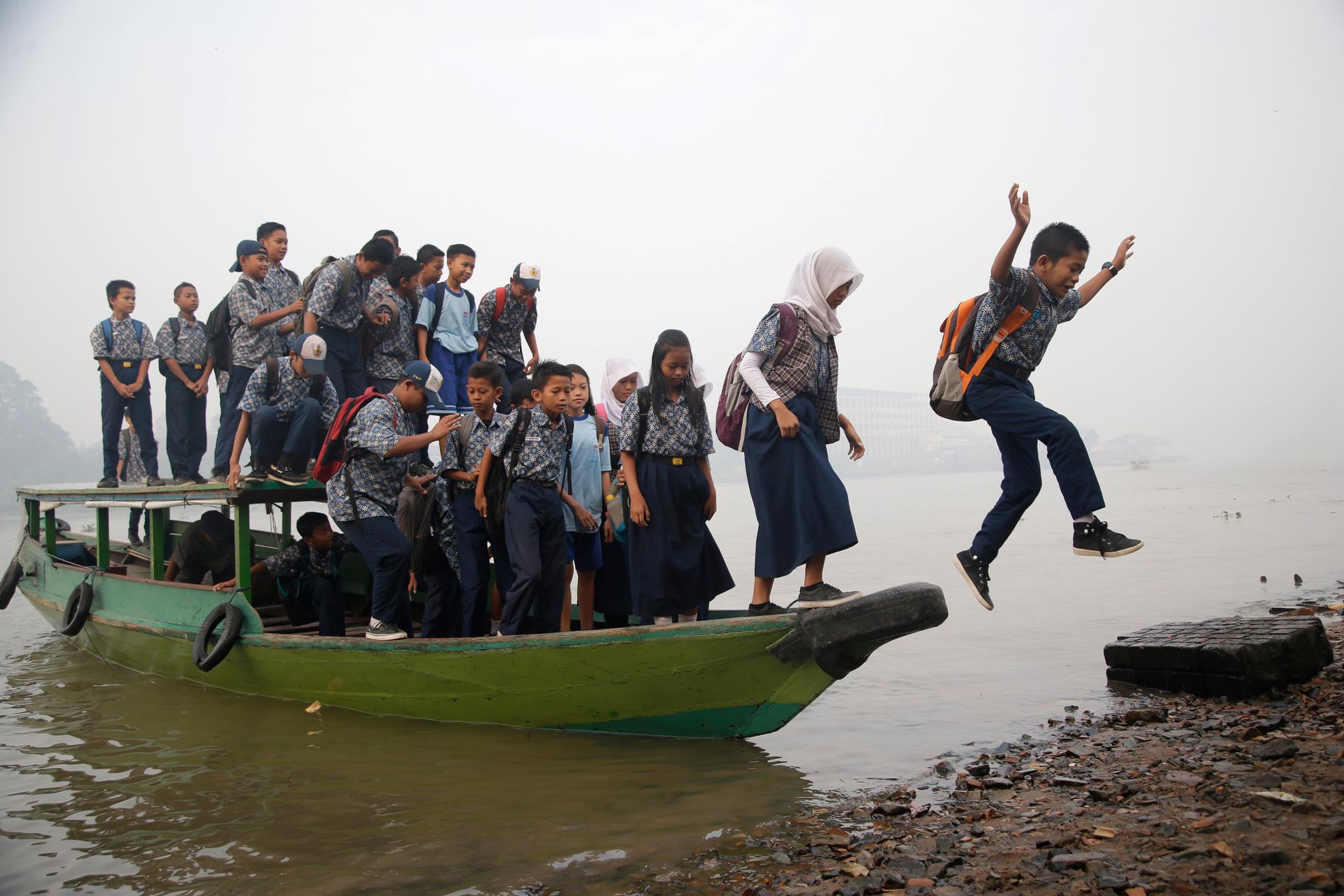 Elever hoppar i land på väg till skolan vid Musiflodeni i södra Sumatra.
