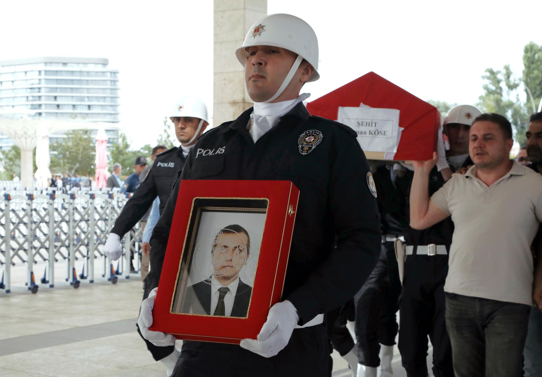 En polis bär en bild av den turkiske diplomaten Osman Köse som mördades i Erbil i Irak inför begravningen i Turkiets huvudstad Ankara.