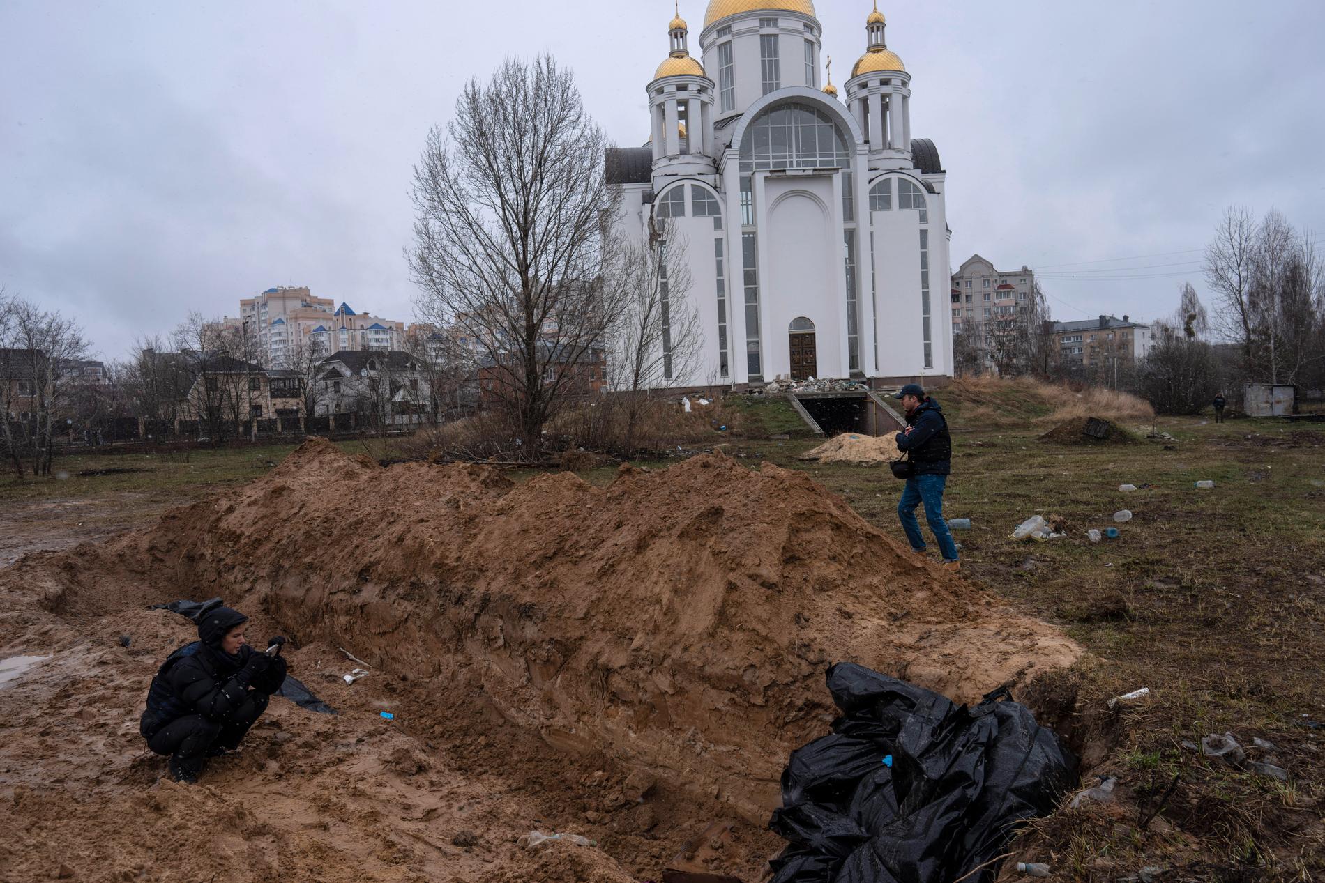 Journalist fotar massgraven intill Sankt Andreas kyrka i Butja under söndagen.