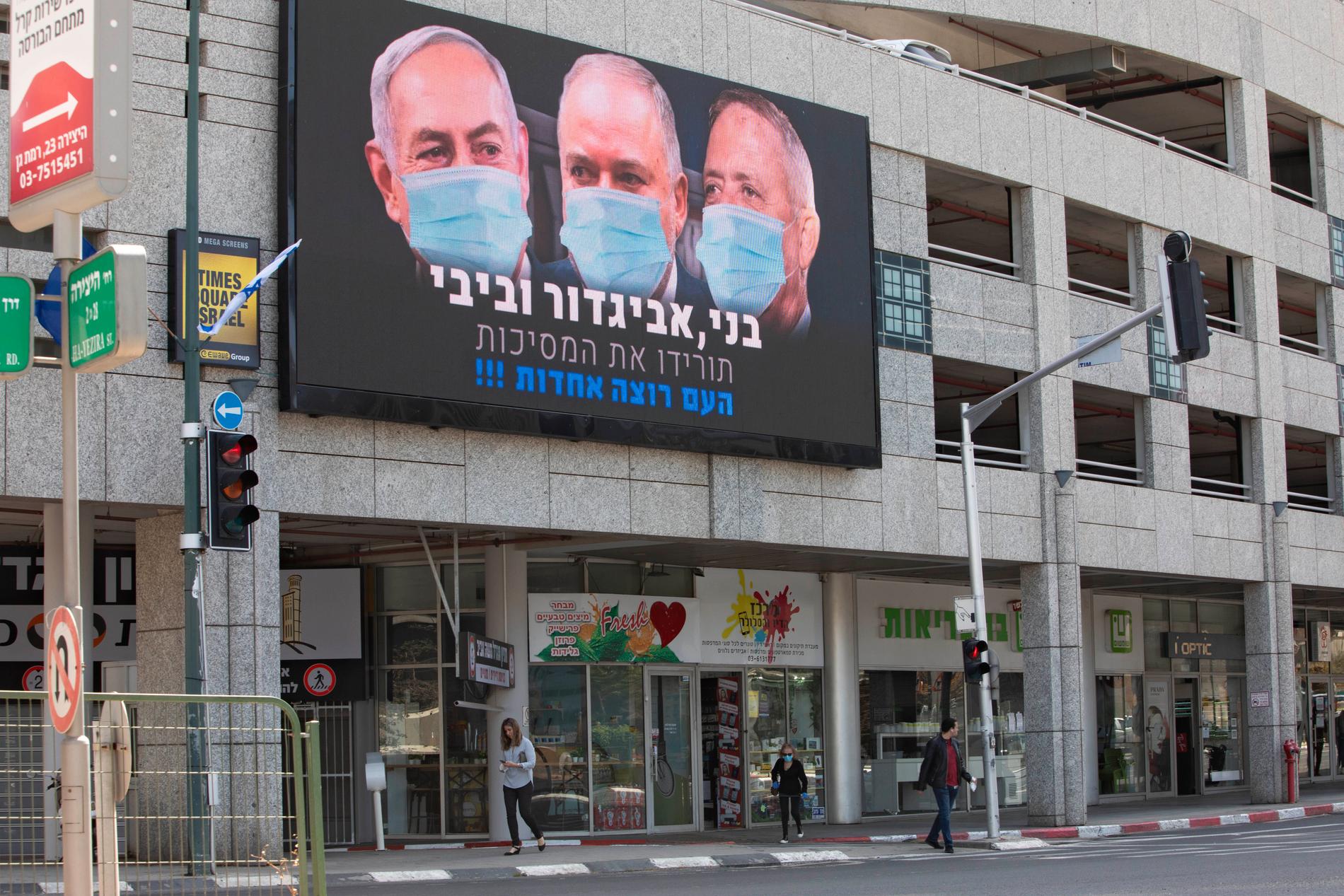 Israels premiärminister Benjamin Netanyahu isolerar sig efter att möjligen ha kommit i kontakt med en smittad medarbetare vid ett knesset-sammanträde. Skylten på bilden sitter i Tel Aviv och visar Netanyahu och ledarna för de två främsta oppositionspartierna, Benny Gantz och Avigdor Lieberman.