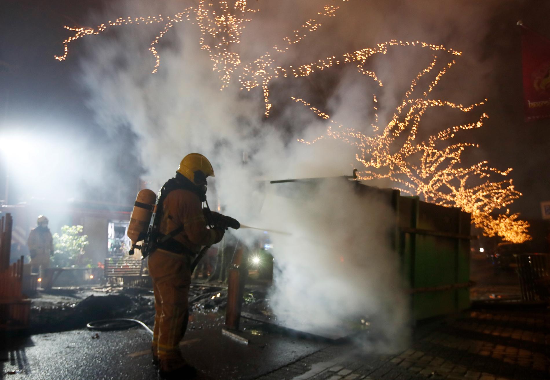 Räddningstjänsten släcker en container som satts i brand under protesterna mot utegångsförbudet.