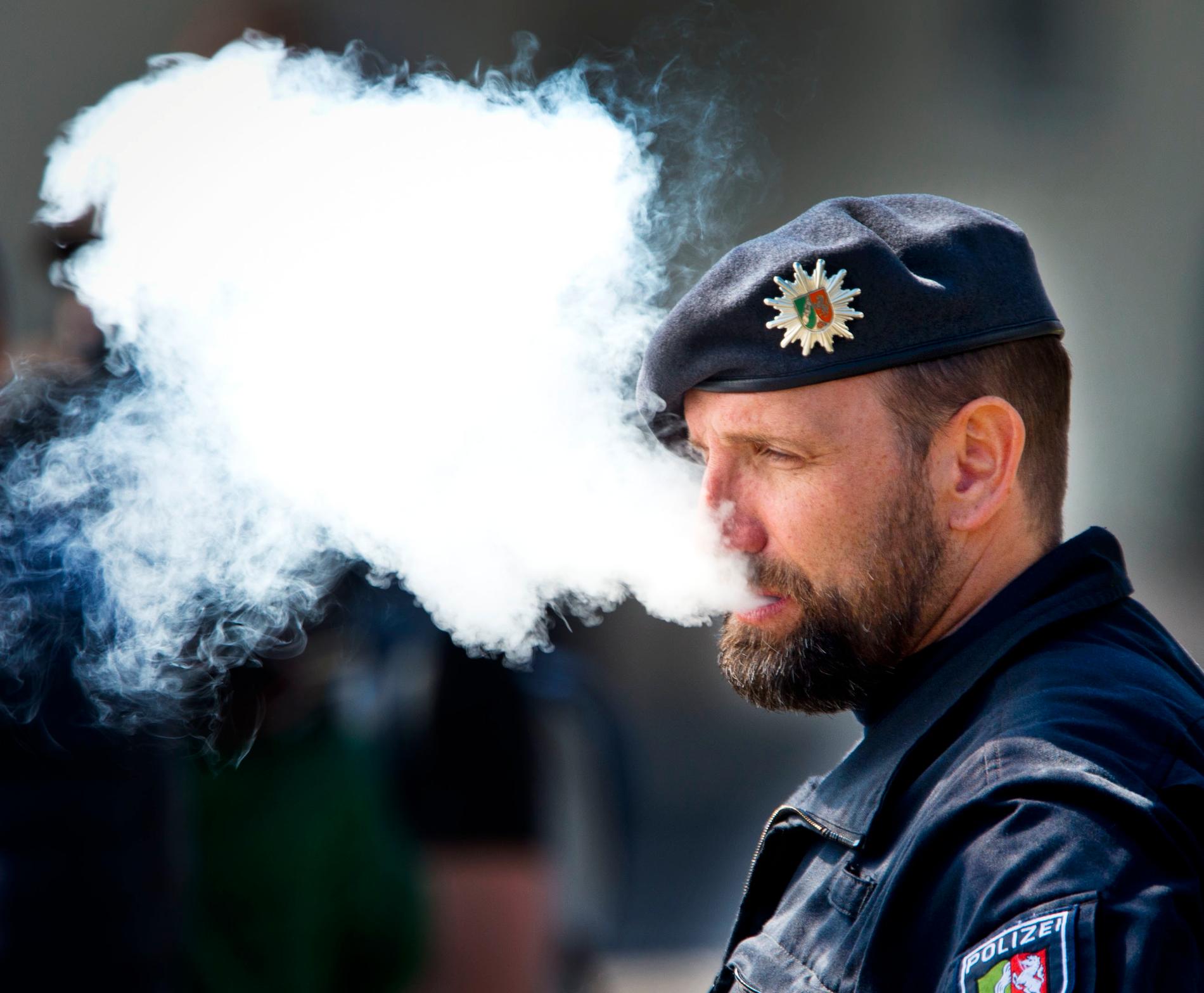 En polisman blåser ut rök från en e-cigarett under ceremonin då Karl Marx-statyn avtäcktes i tyska Trier på lördagen.