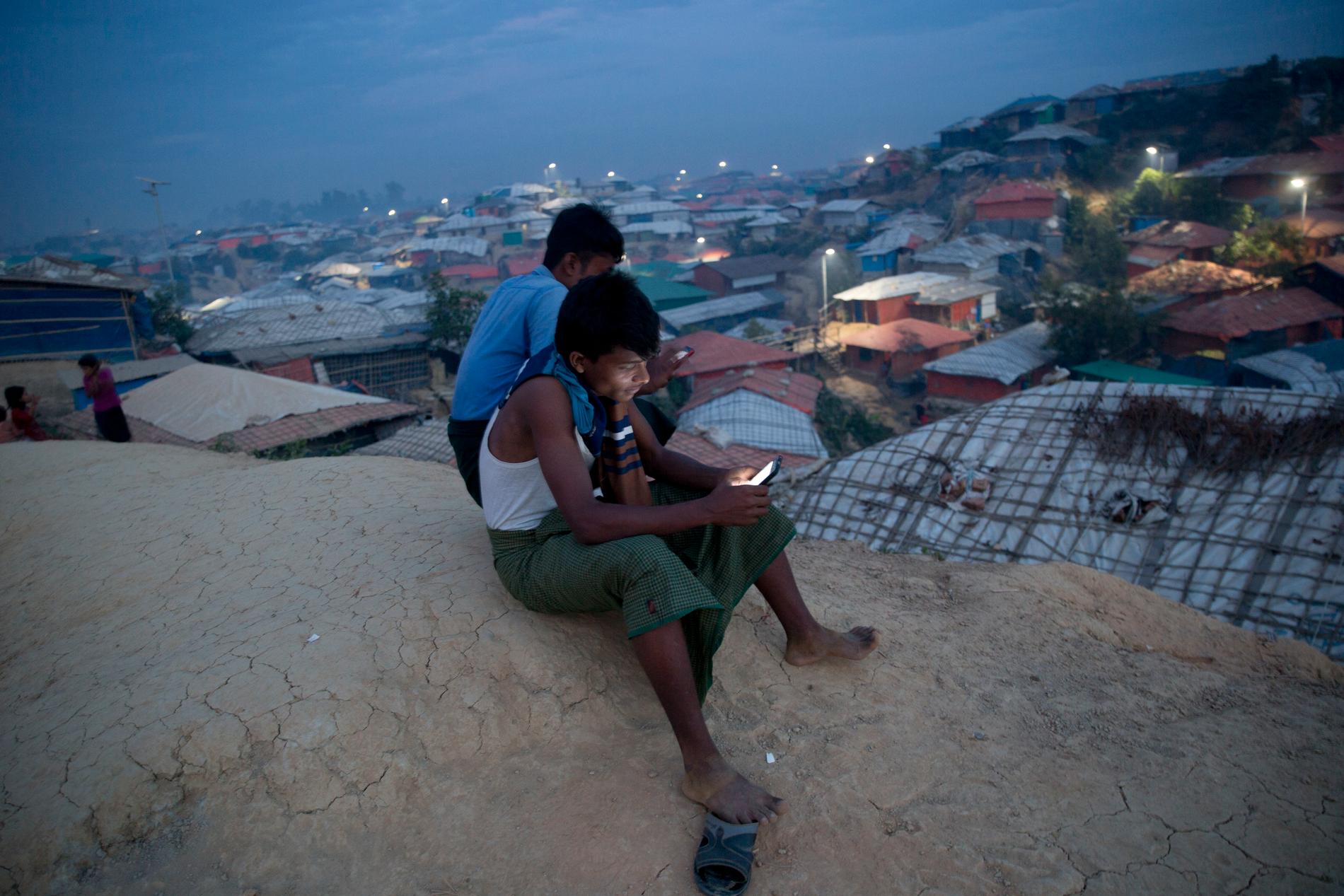 Två män använder sina mobiltelefoner på en klippa ovanför flyktinglägret Balukhali i Bangladesh. Arkivbild.