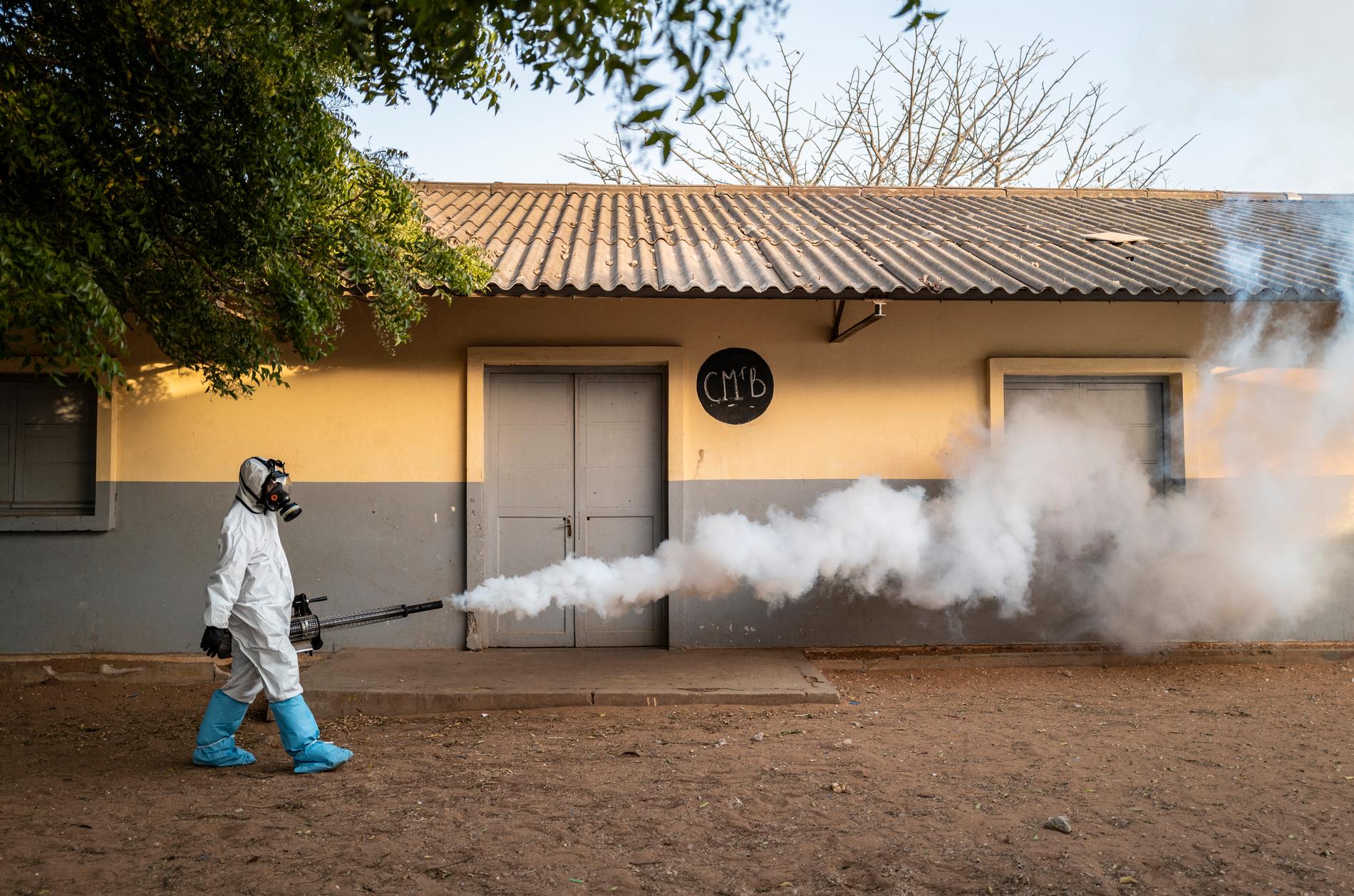 Byn Ngunta ligger både i Senegal och i Gambia. Båda länderna har drabbats av coronaviruset. På bilden ses en kommunanställd som sprutar desinfektionsmedel utanför en skola i Dakar i Senegal.
