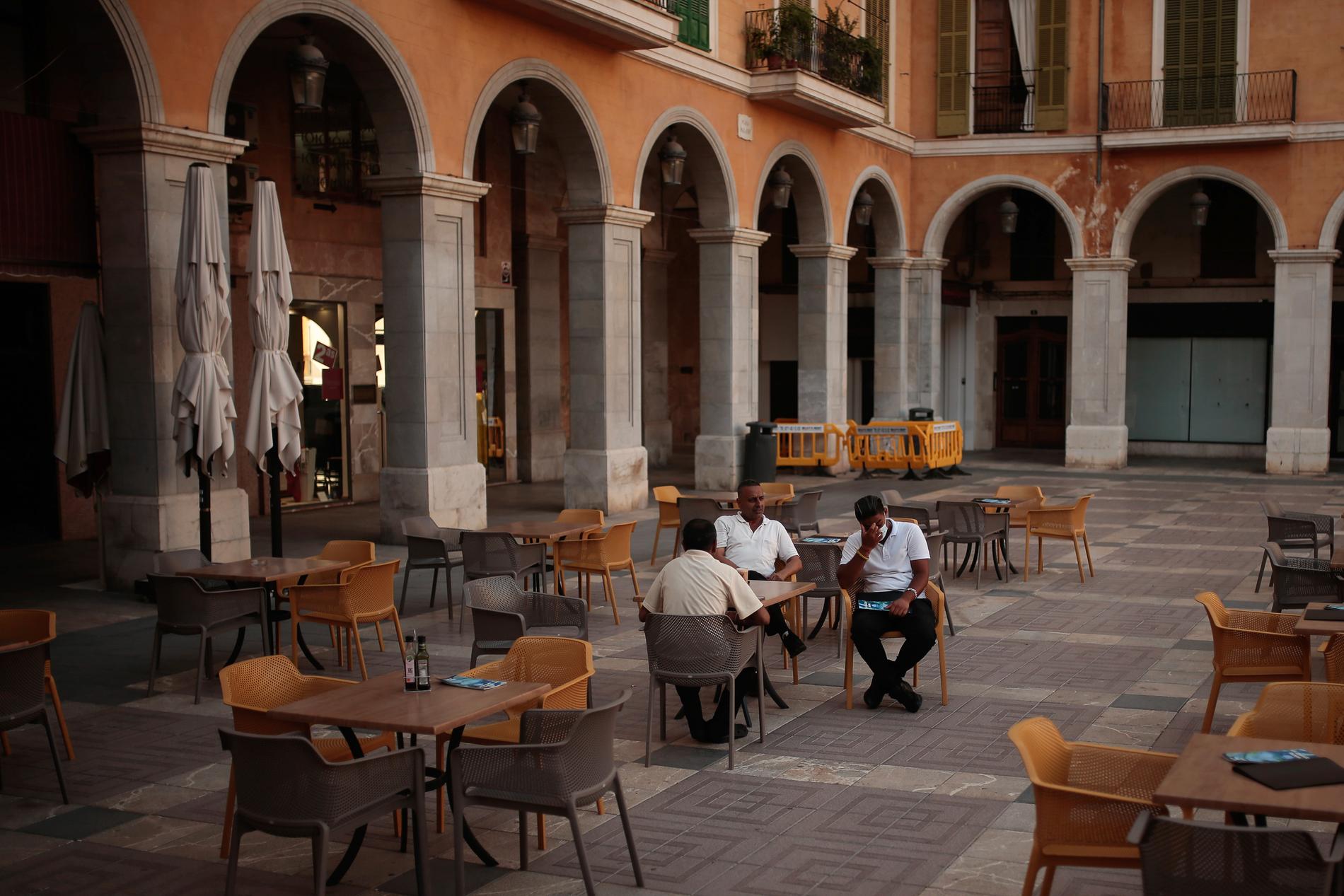 Män på ett folktomt restaurangtorg på Mallorca. 