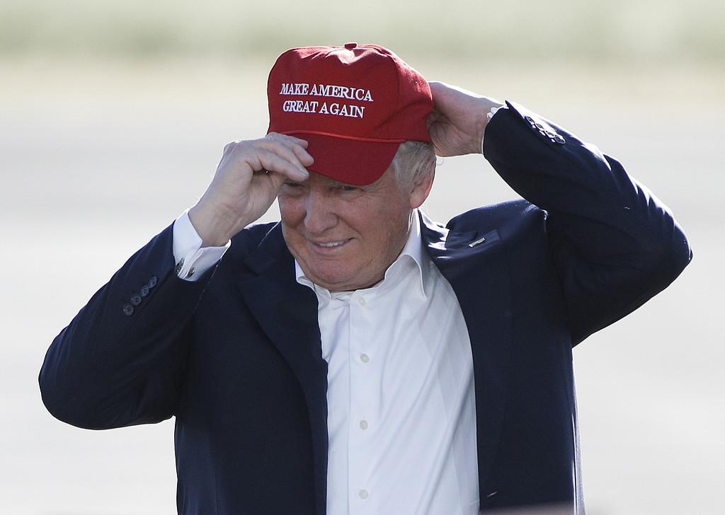 Donald Trump tar på sig en keps med texten ”Make America great again”.