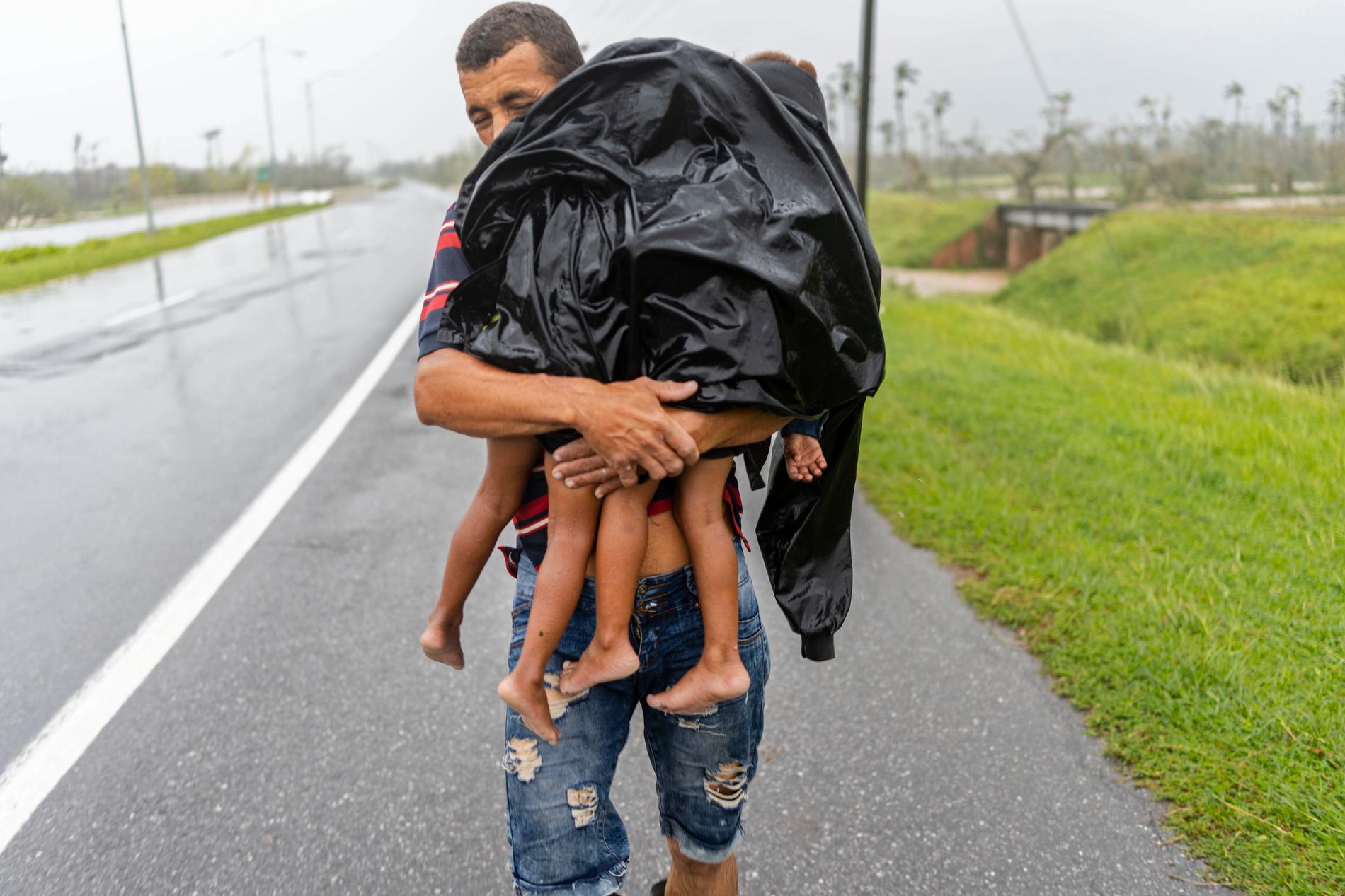 En man bär två barn i regnet i jakt på skydd efter att orkanen Ian svämmat över deras hus.