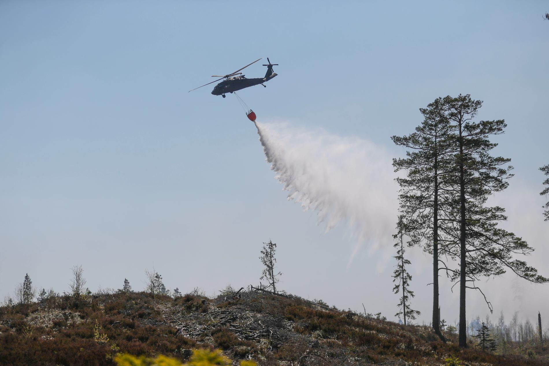 Försvarets helikopter hämtar vatten i en sjö för att vattenbomba en skogsbrand norr om Tjällmo, norr om Motala i Östergötland under tisdagen.