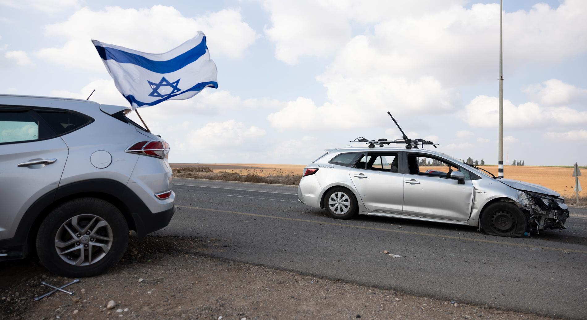 Övergivna bilar längs vägen. En Israelisk flagga med kulhål vajar i vinden.