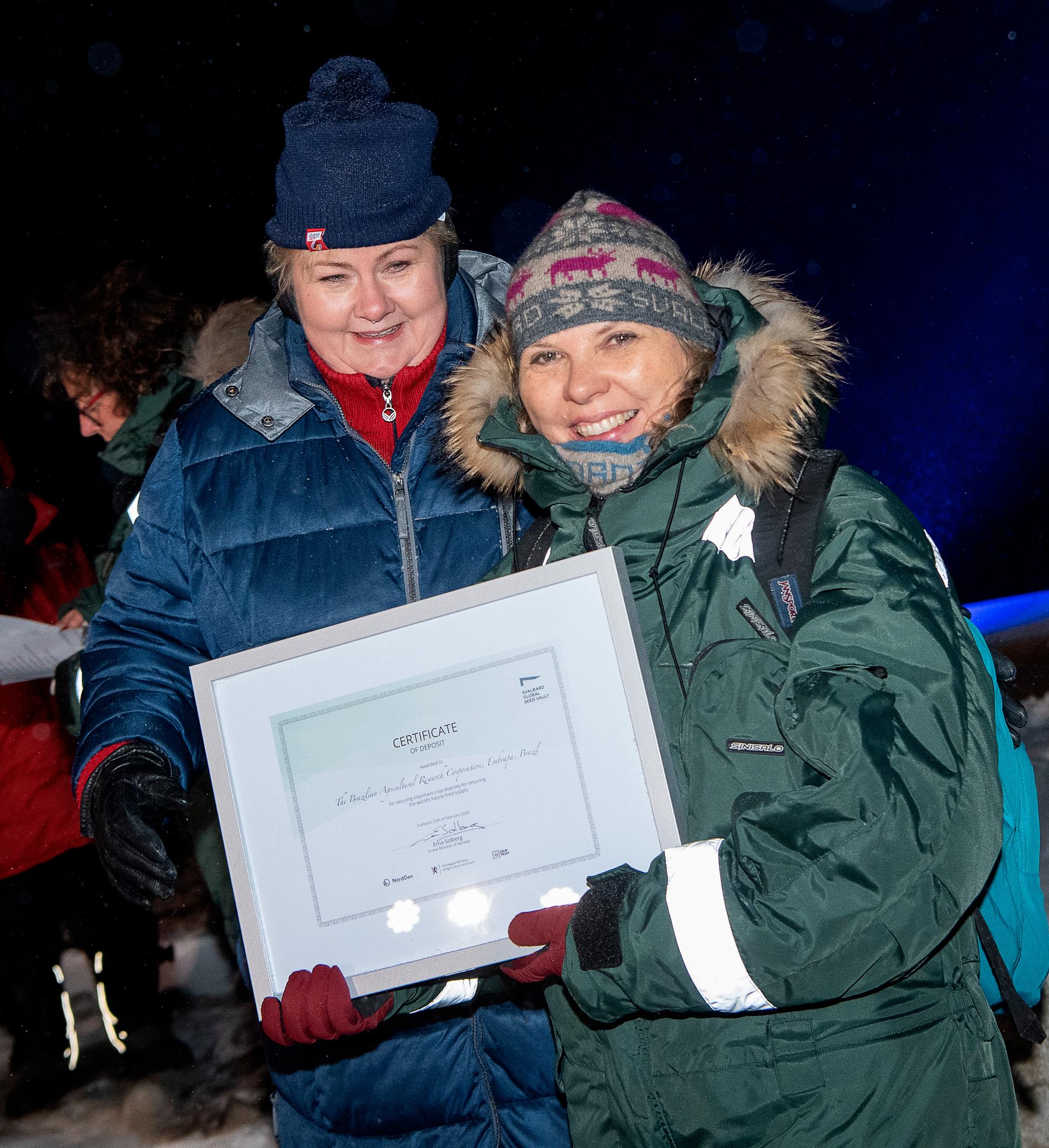 Norges statsminister Erna Solberg delar ut certifikat till Rosa Lía Barbieri från den brasilianska genbanken Embrapa vid tisdagskvällens frödeponeringsceremoni utanför Svalbards globala frövalv i Longyearbyen.