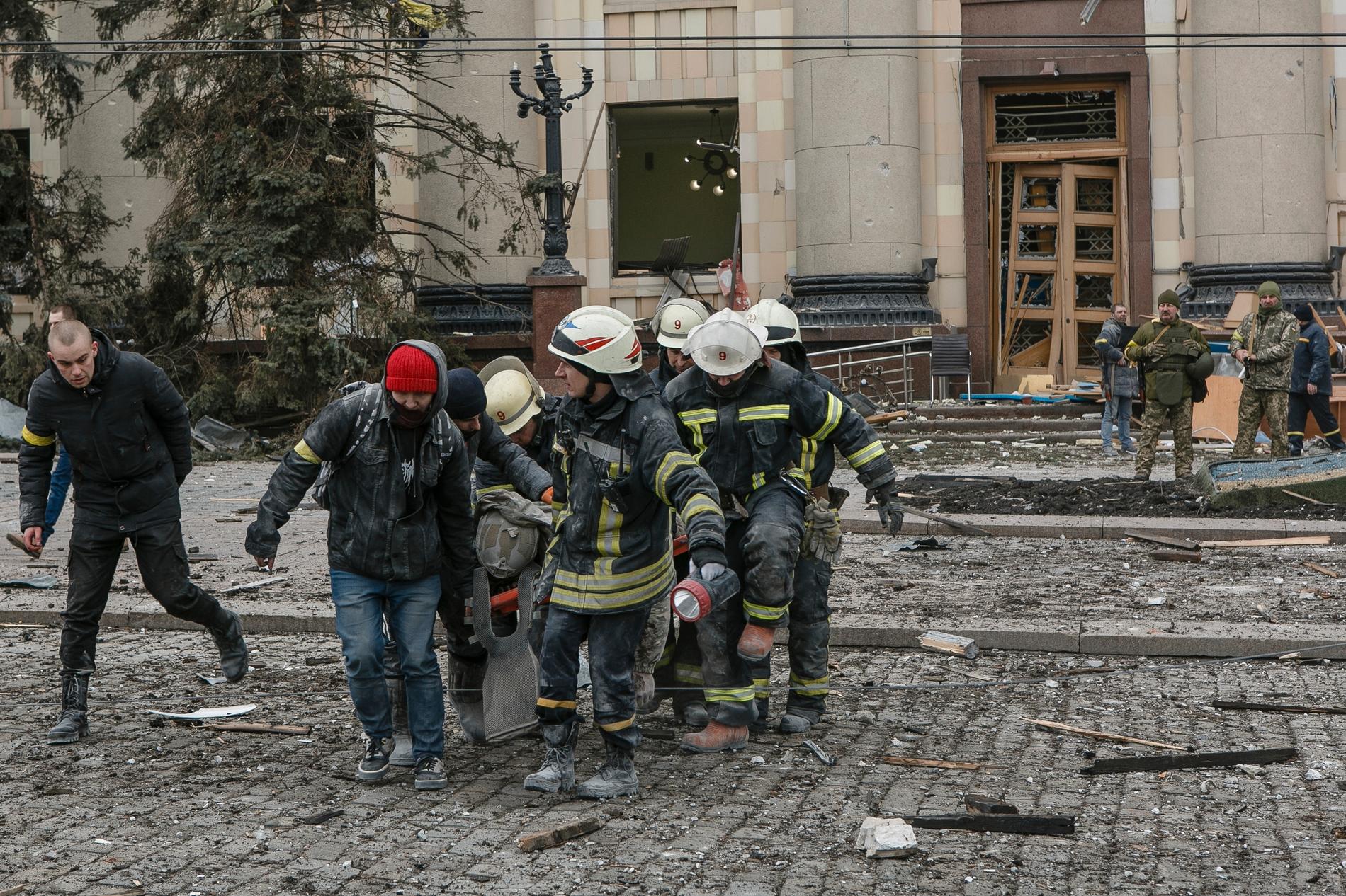 Ukrainska räddningsarbetare bär en person som skadats i attacken mot stadshuset i Charkiv.