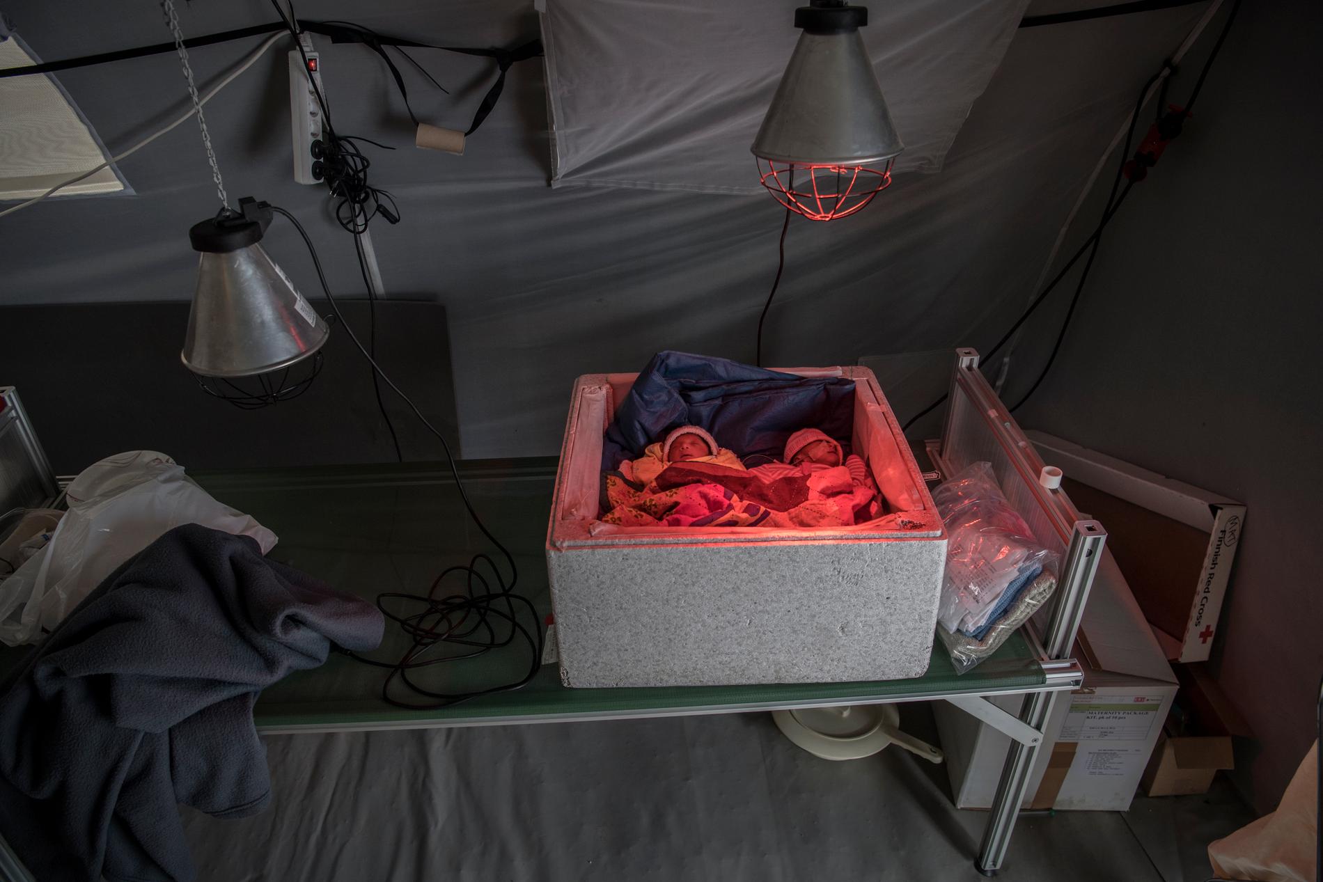 Två nyfödda tvillingflickor har lagts i en frigotlitlåda och får värme från en hemmasnickrad värmelampa på Röda korsets fältsjukhus utanför Kutupalonglägret.