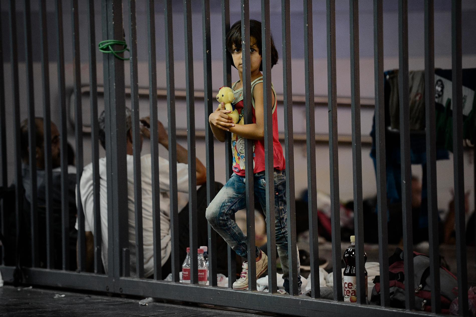 7-åriga Rinad från Allepo i Syrien hänger mot staketet som hindrar flyktingar för att ta sig till tåget.